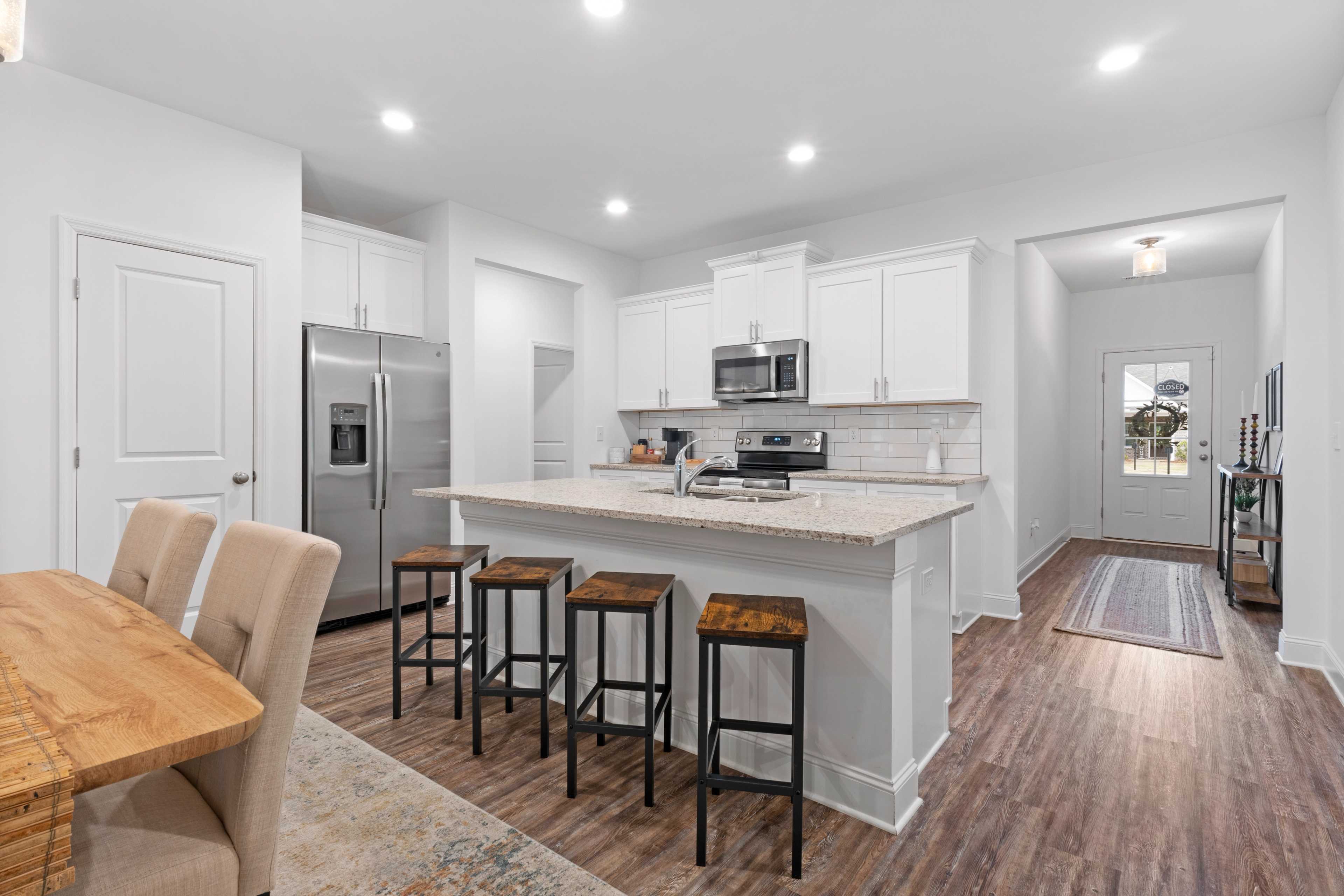 Open-concept kitchen and dining at The Retreat at Hollon Meadow in Decatur, Alabama with white cabinets, stainless appliances, large island, hardwood floors