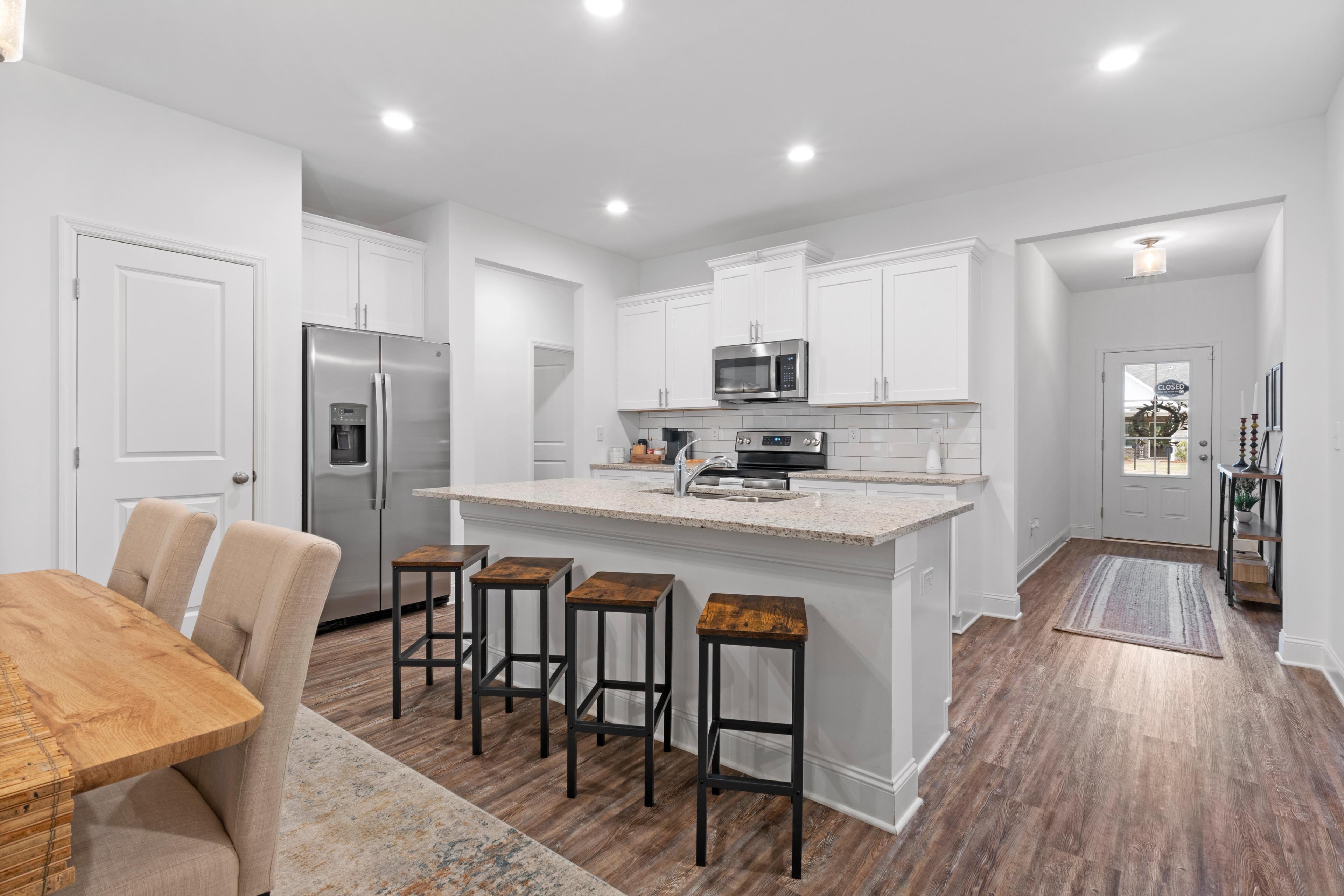 Spacious open-concept kitchen and dining in The Cumberland B with white cabinets, large island, stainless appliances, hardwood floors