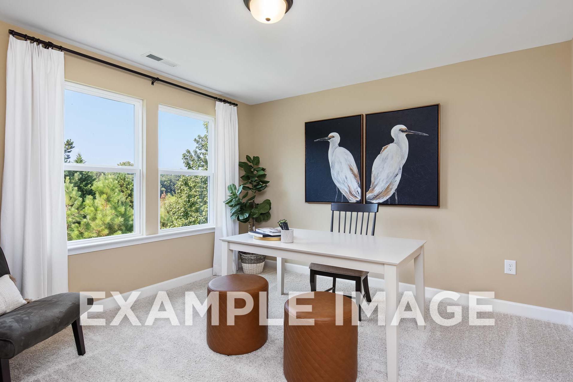 Spacious home office in The Willow E featuring beige walls, large windows with tree views, egret artwork, and modern desk