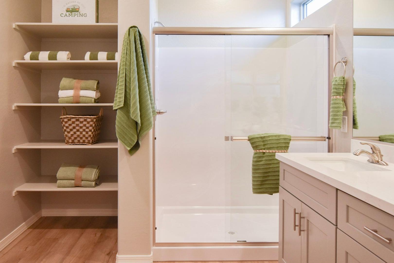Spacious master bathroom in The Harmony B featuring open linen shelves, glass shower enclosure, and modern gray vanity