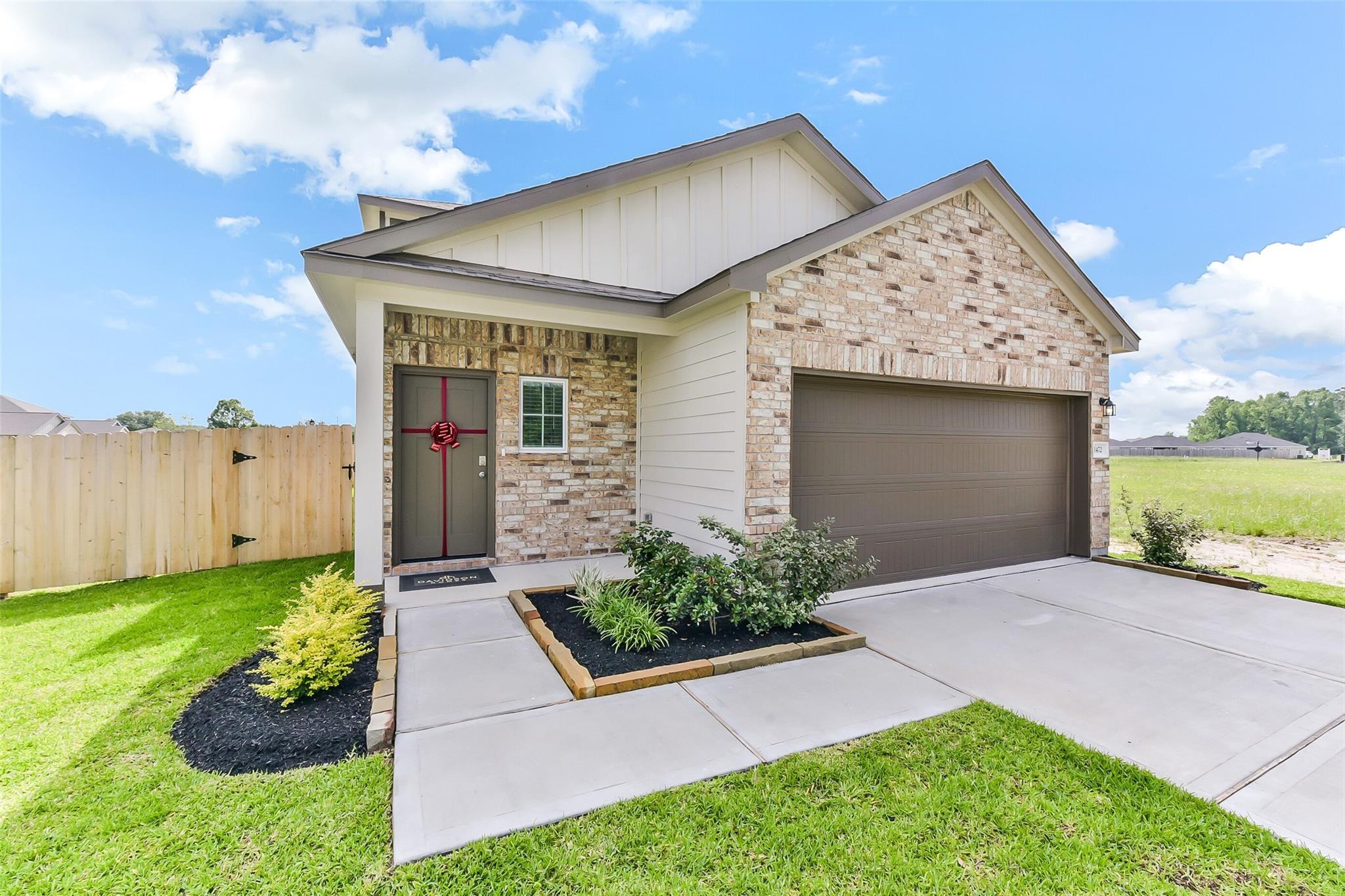 Two-story brick and siding home with 2-car garage, red bow front door, landscaped yard in The Villages at WestPointe, Dayton, Texas