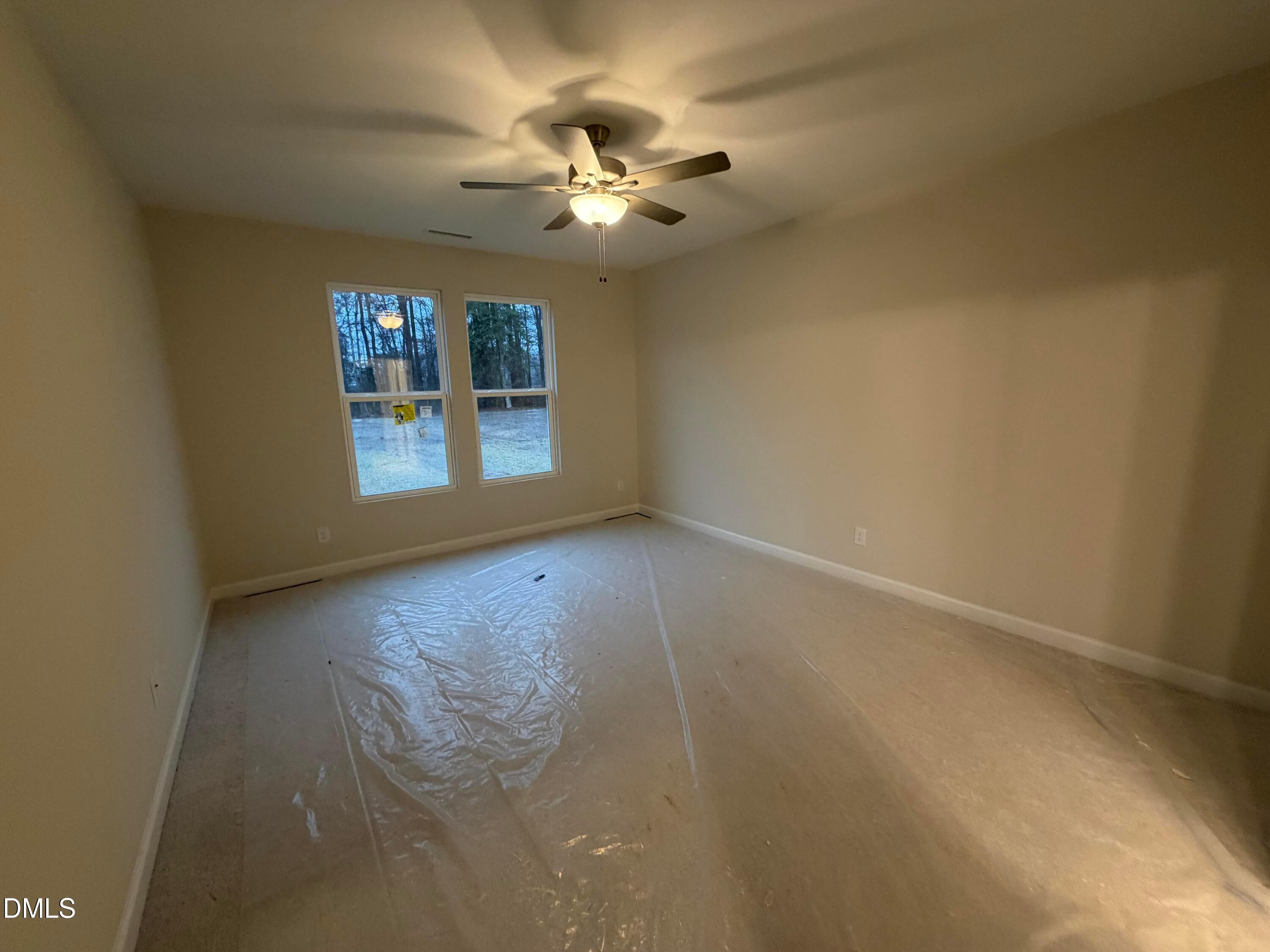 Bright empty bedroom with large windows overlooking woods, ceiling fan, and protective flooring in Davidson Homes The Daphne C, Lillington NC