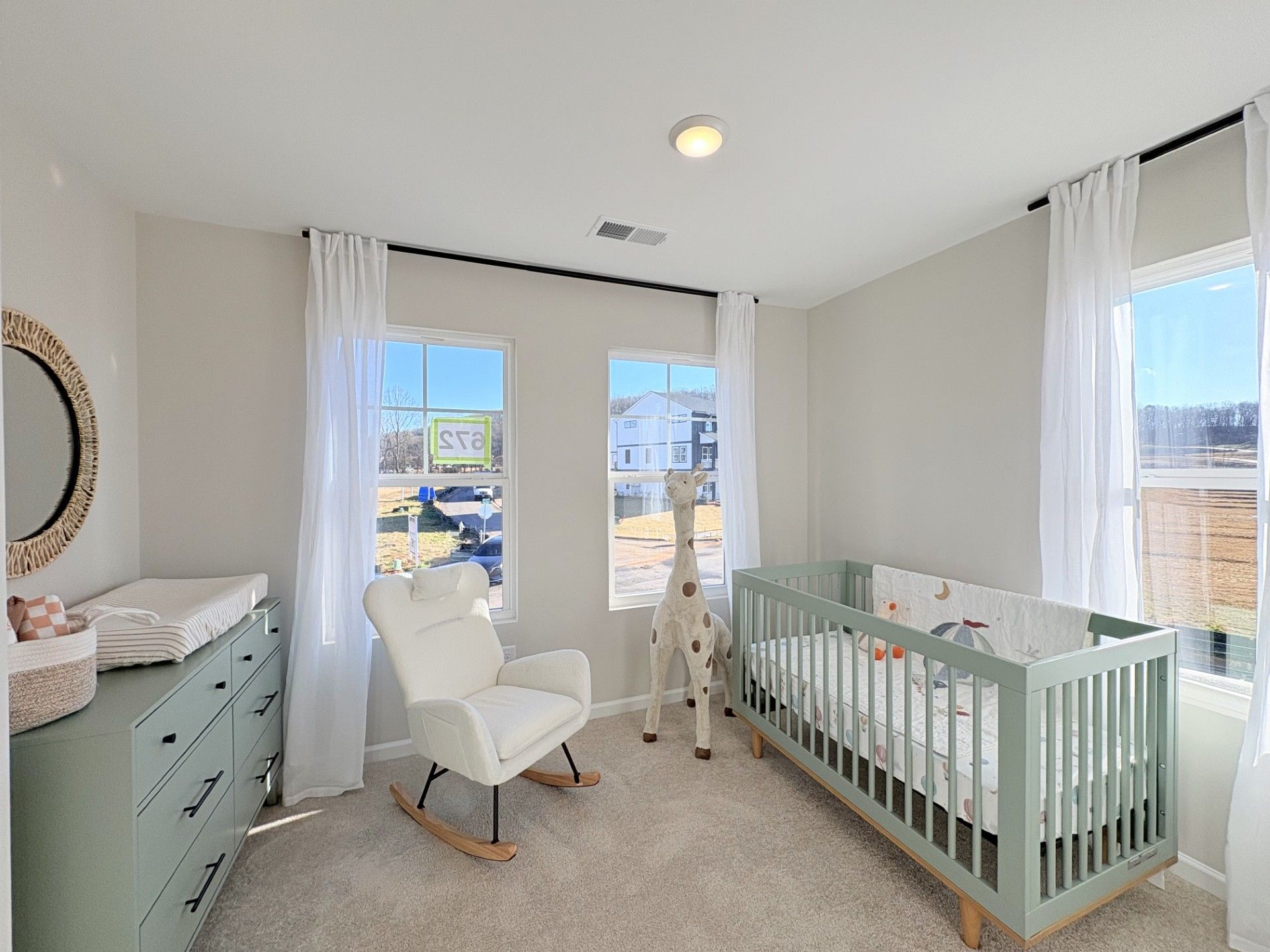 Cozy nursery in Hemingway Cumming GA with green crib, white rocking chair, giraffe toy, and sheer-curtained windows by Davidson Homes