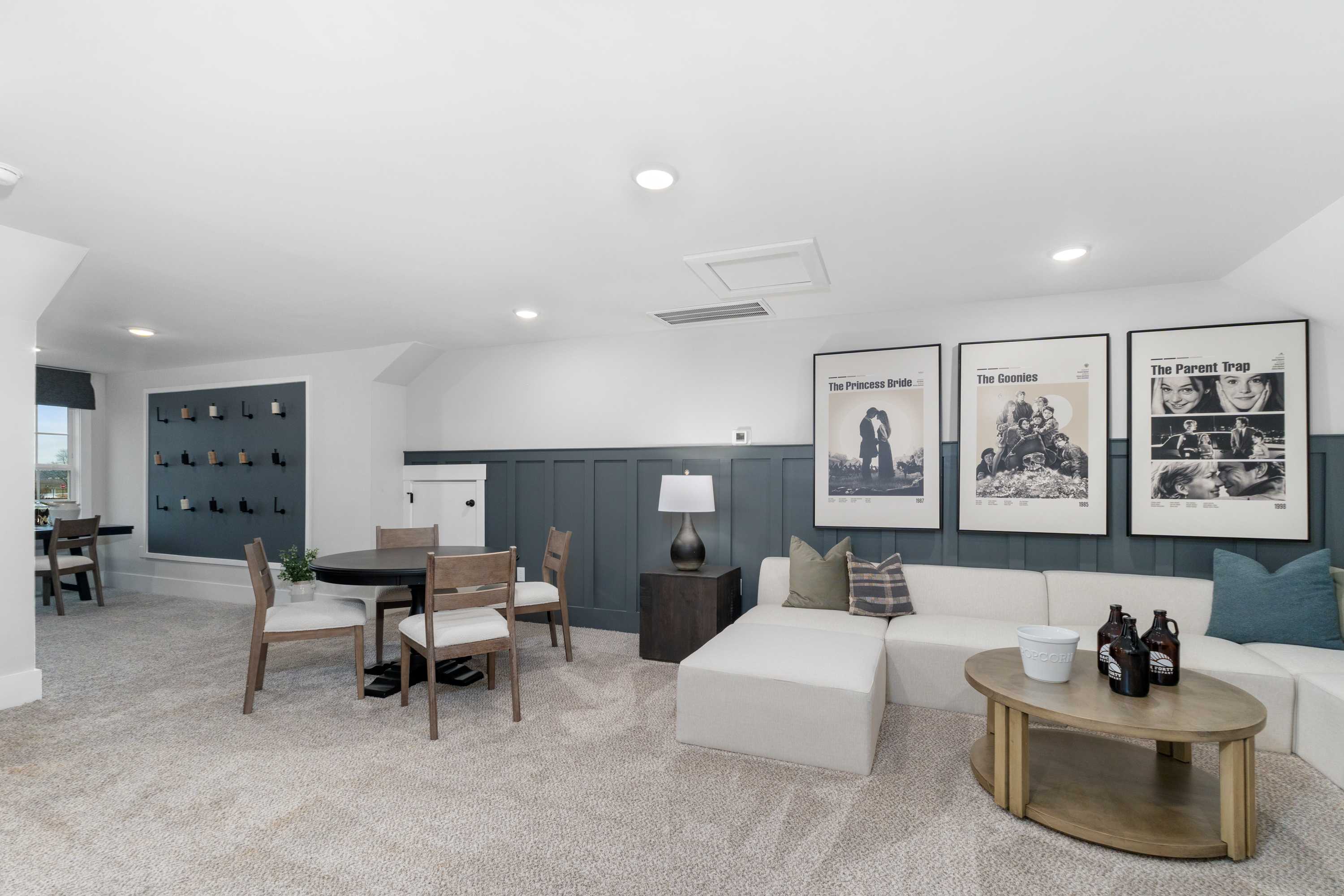 Spacious bonus room at Kendall Farms in Toney Alabama with white sectional sofa, round wooden table, black-and-white gallery wall art, and wine shelves