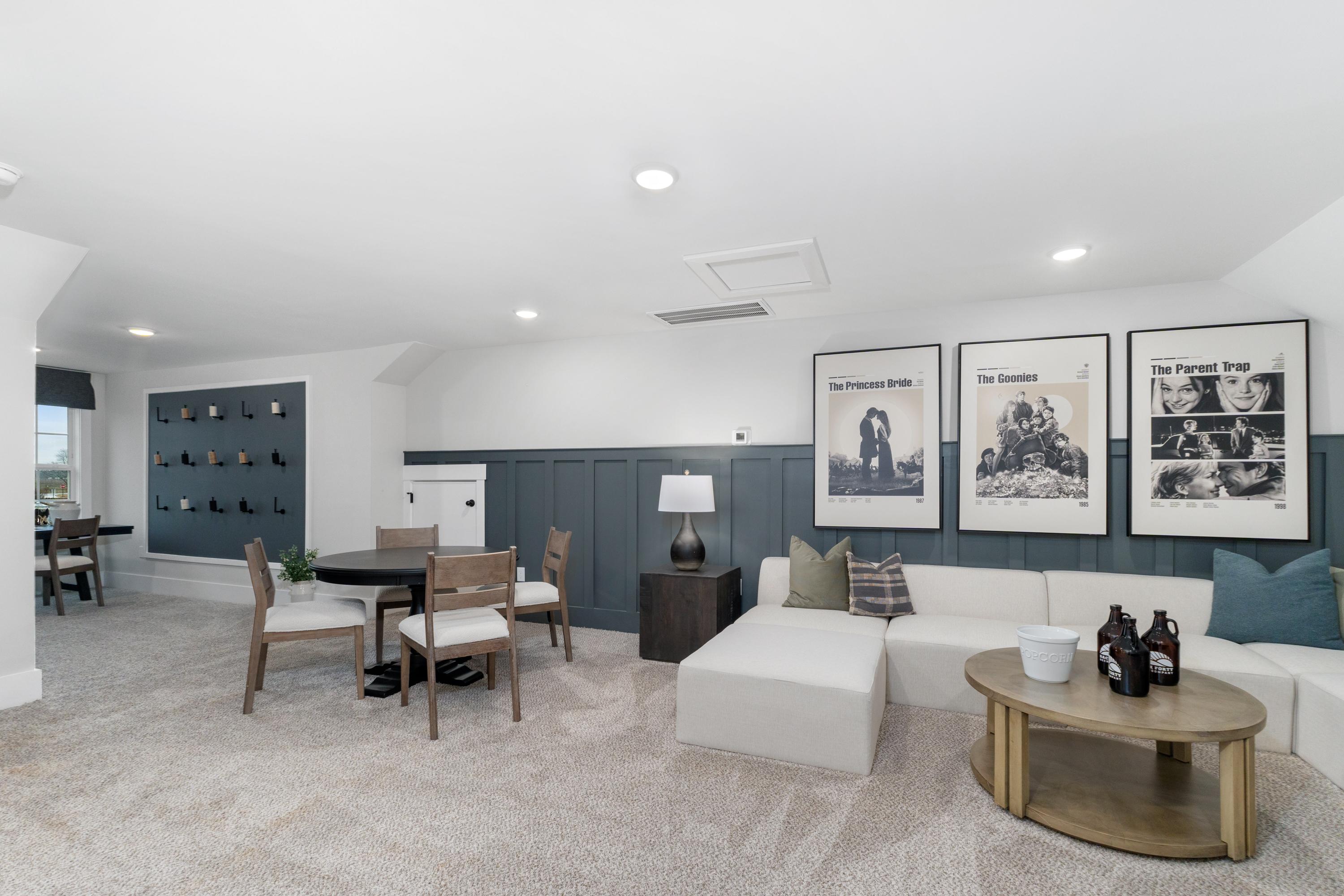 Spacious bonus room at Kendall Farms in Toney Alabama with white sectional sofa, round wooden table, black-and-white gallery wall art, and wine shelves