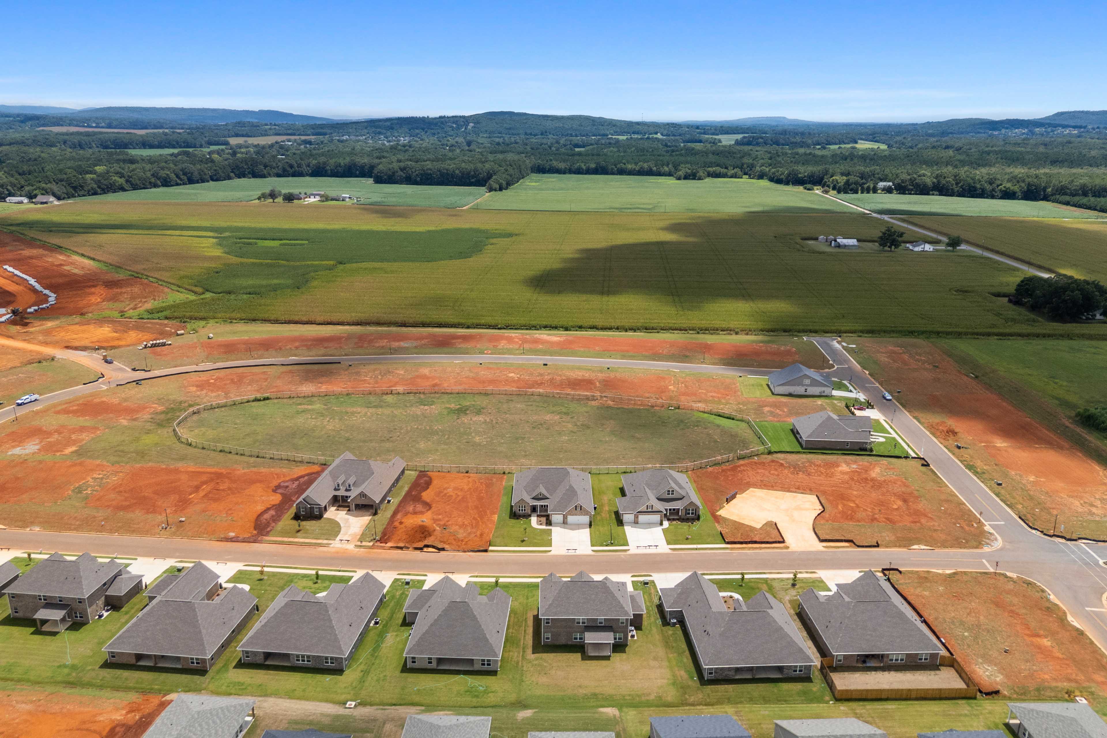 Aerial view of new shingled-roof homes in Kendall Farms Toney Alabama amid construction sites and farmland