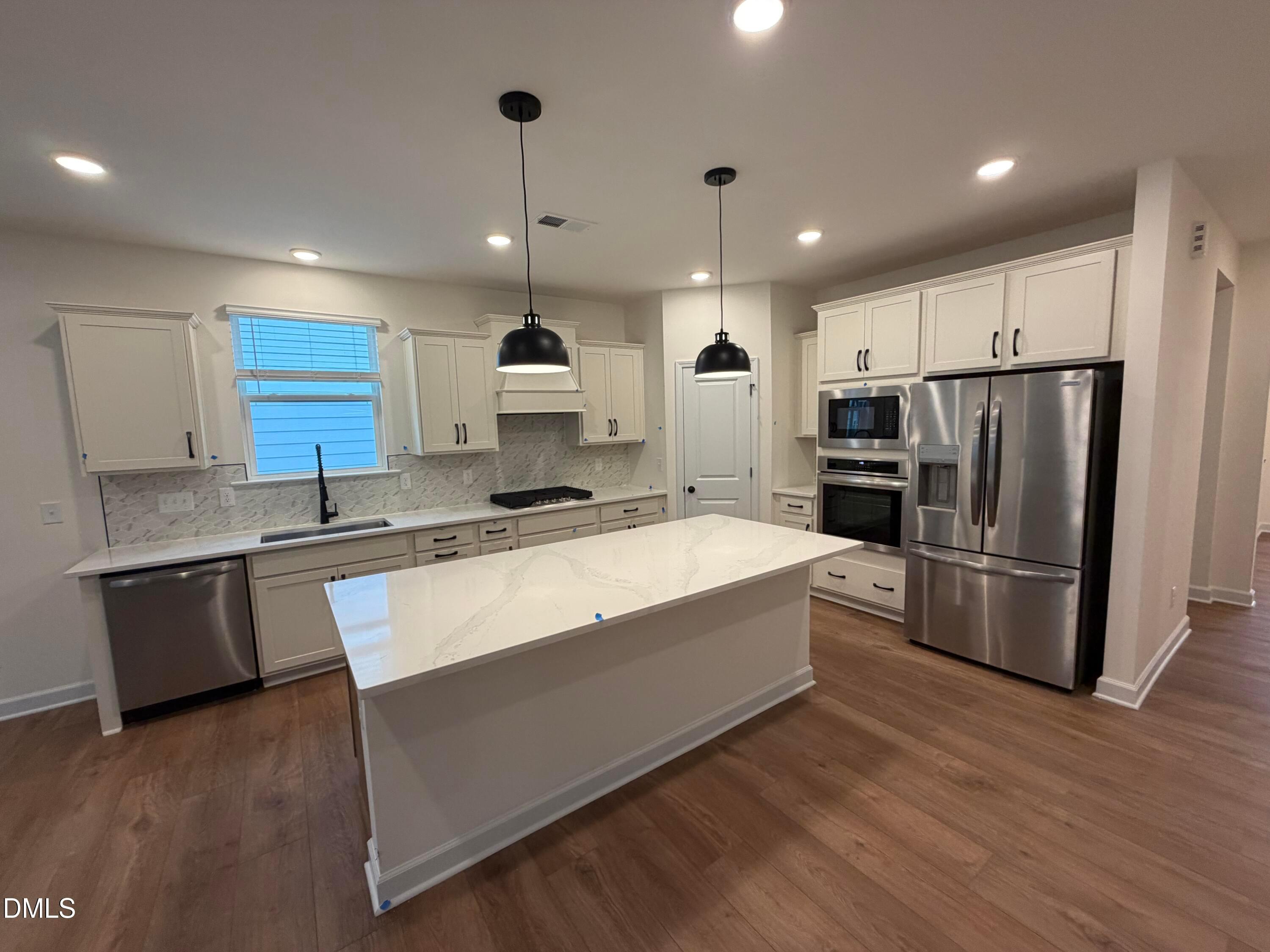 Modern kitchen with white cabinetry, quartz island, pendant lights, and stainless appliances in Davidson Homes Ashport M, Wendell NC