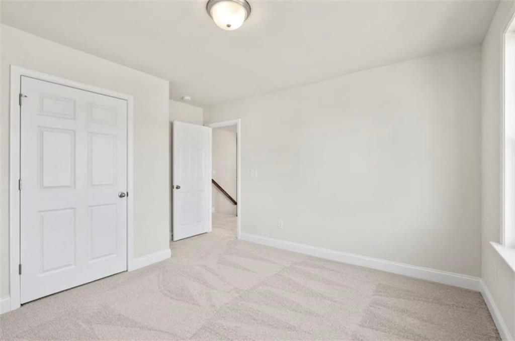 Bright, neutral-toned bedroom with plush carpet in The Ash C floor plan at Wehunt Meadows in Hoschton, Georgia.
