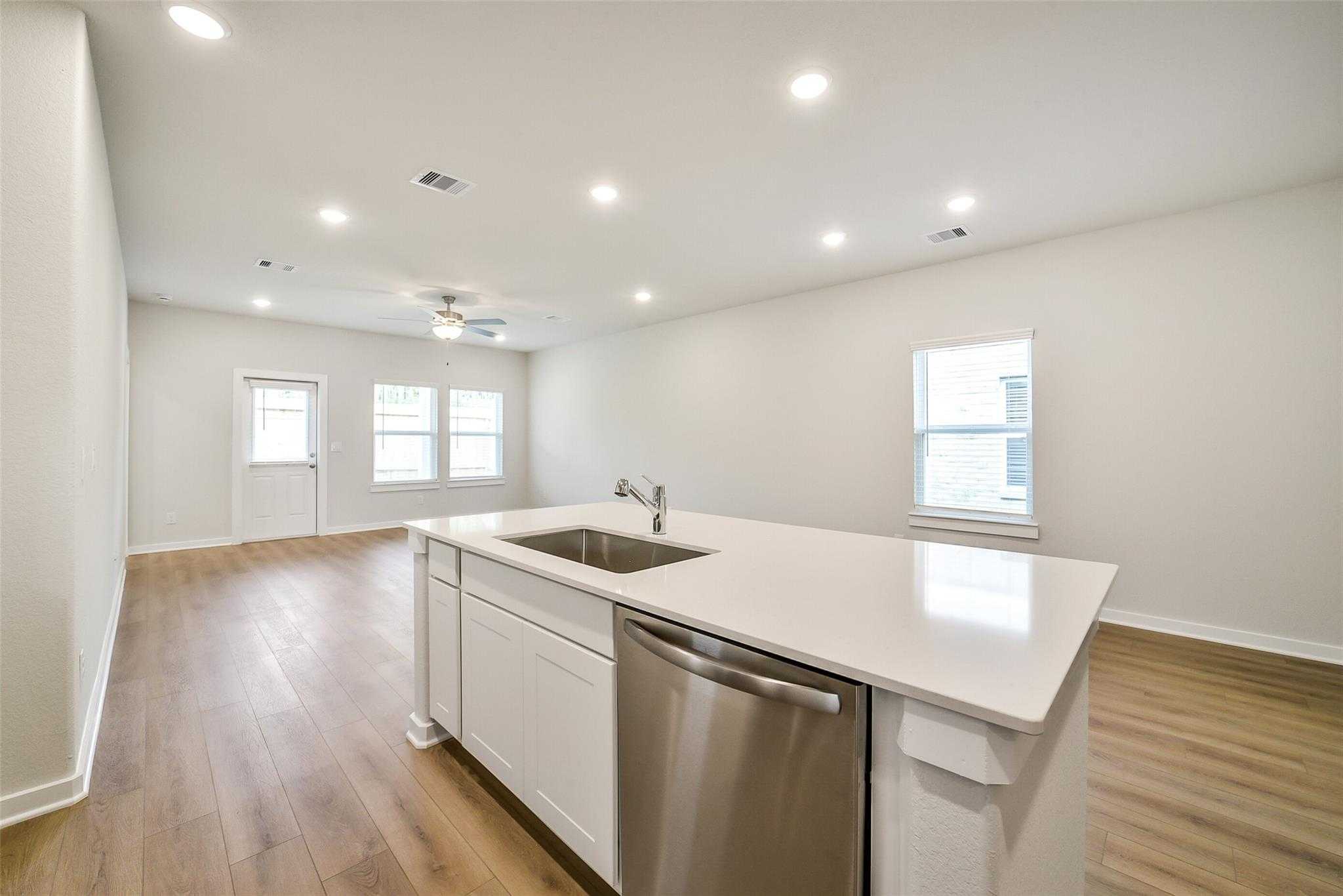 Modern open-concept kitchen with white island, sink, dishwasher, hardwood floors in Davidson Homes The Blanco E, Magnolia Texas