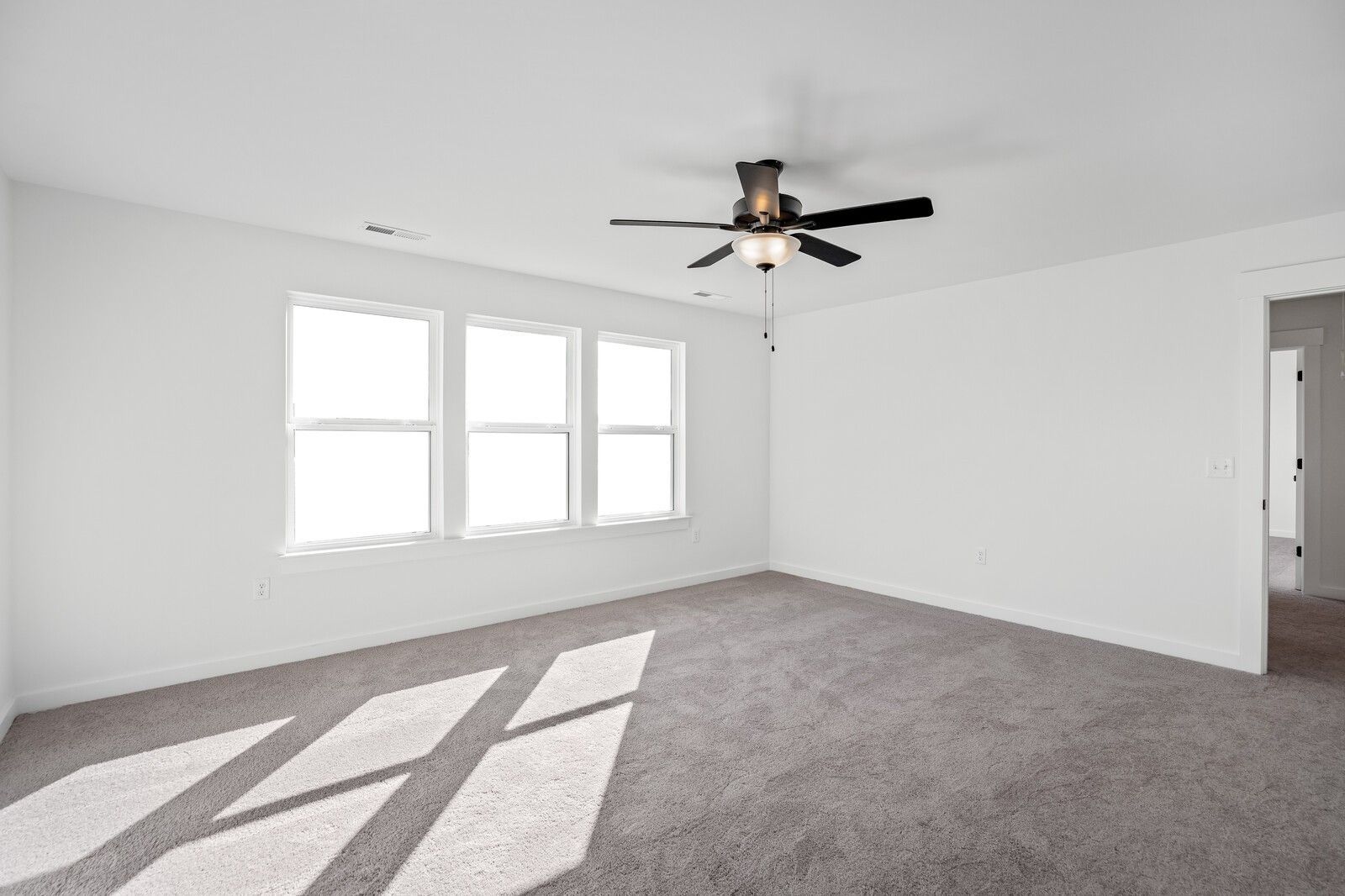 Bright bedroom with large windows, sunlight on beige carpet, and ceiling fan in Davidson Homes The Willow C, Gallatin, TN