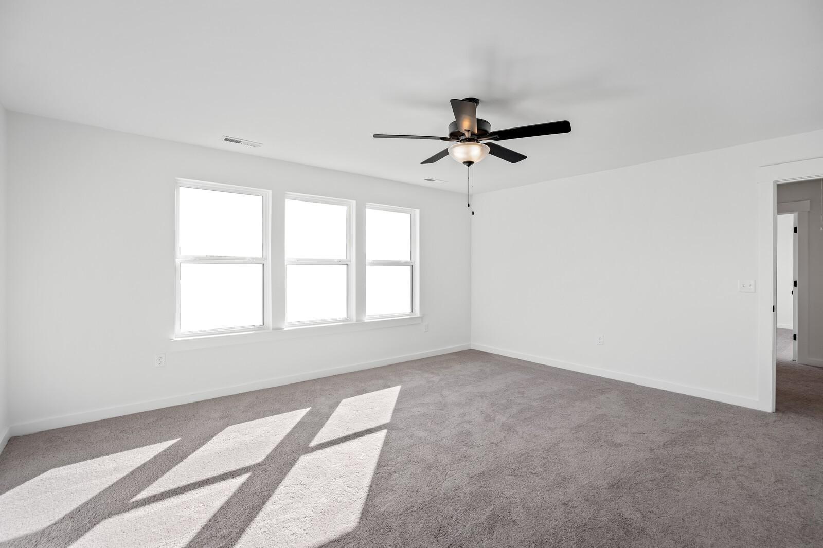 Bright bedroom with large windows, sunlight on beige carpet, and ceiling fan in Davidson Homes The Willow C, Gallatin, TN