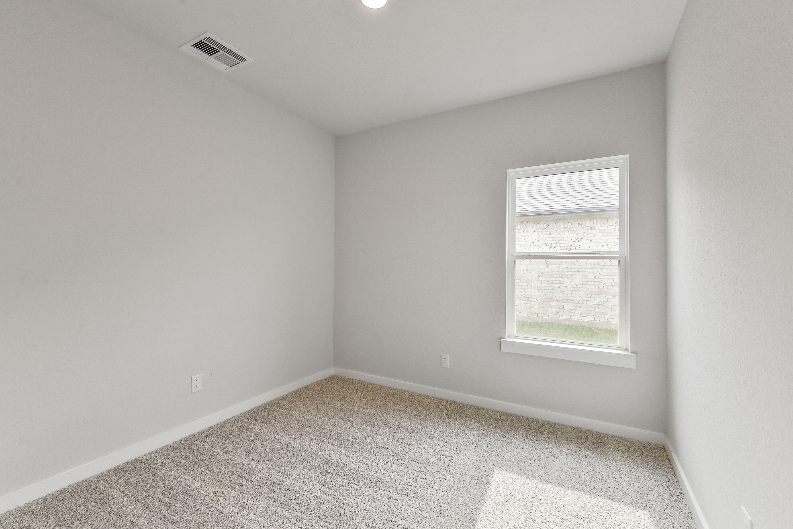 Bright empty bedroom with light gray walls, beige carpet, and window overlooking yard in Davidson Homes The Colorado G, Magnolia Texas