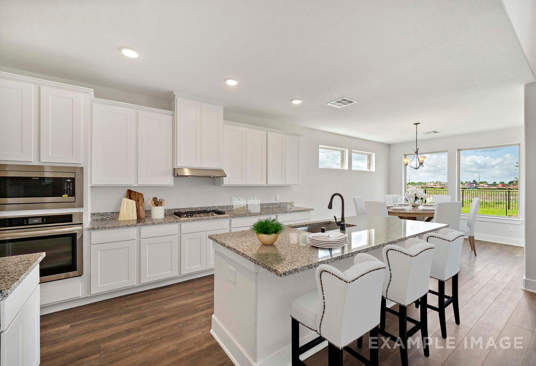 Modern open-concept kitchen in The Victoria A featuring white cabinets, granite island, bar stools, and dining nook with window views
