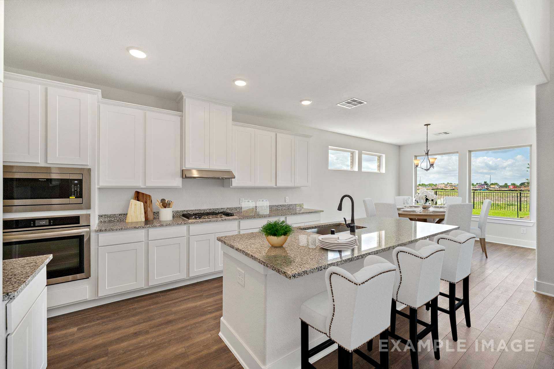 Modern open-concept kitchen in The Victoria A featuring white cabinets, granite island, bar stools, and dining nook with window views