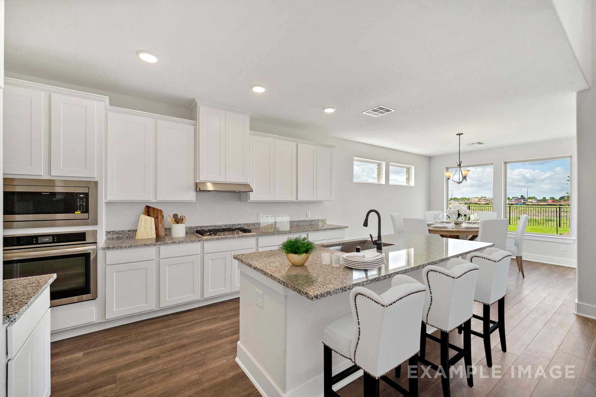 Modern open-concept kitchen in The Victoria A featuring white cabinets, granite island, bar stools, and dining nook with window views