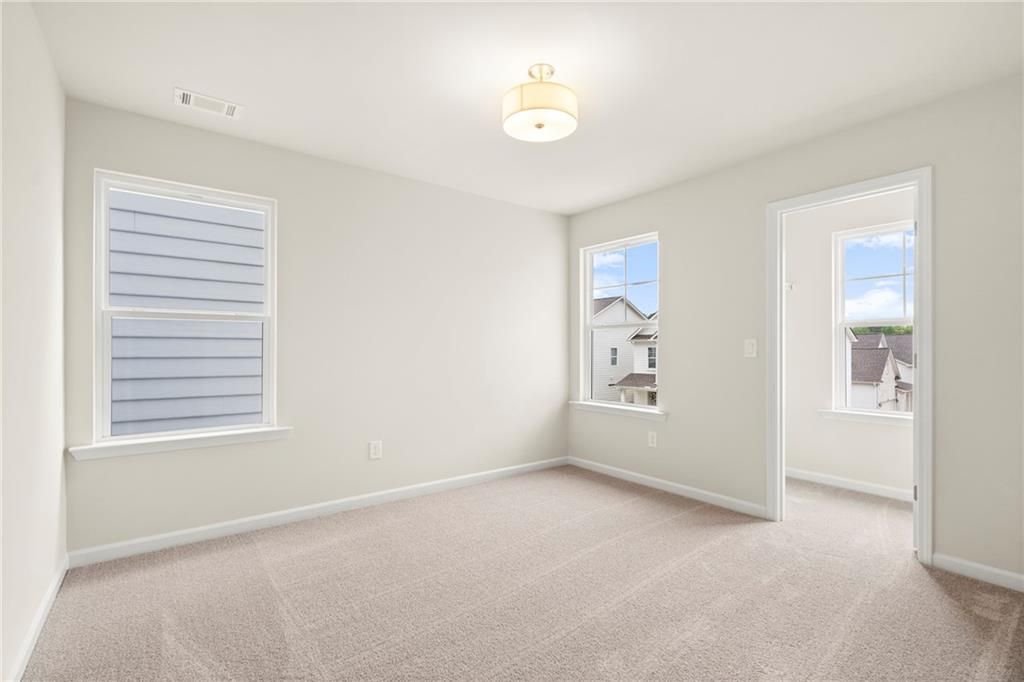 Bright secondary bedroom with beige walls, carpeted floor, large windows, and ceiling fixture in Davidson Homes The Cary A, Kennesaw, Georgia