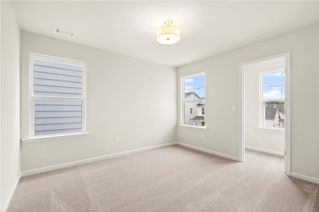 Bright secondary bedroom with beige walls, carpeted floor, large windows, and ceiling fixture in Davidson Homes The Cary A, Kennesaw, Georgia