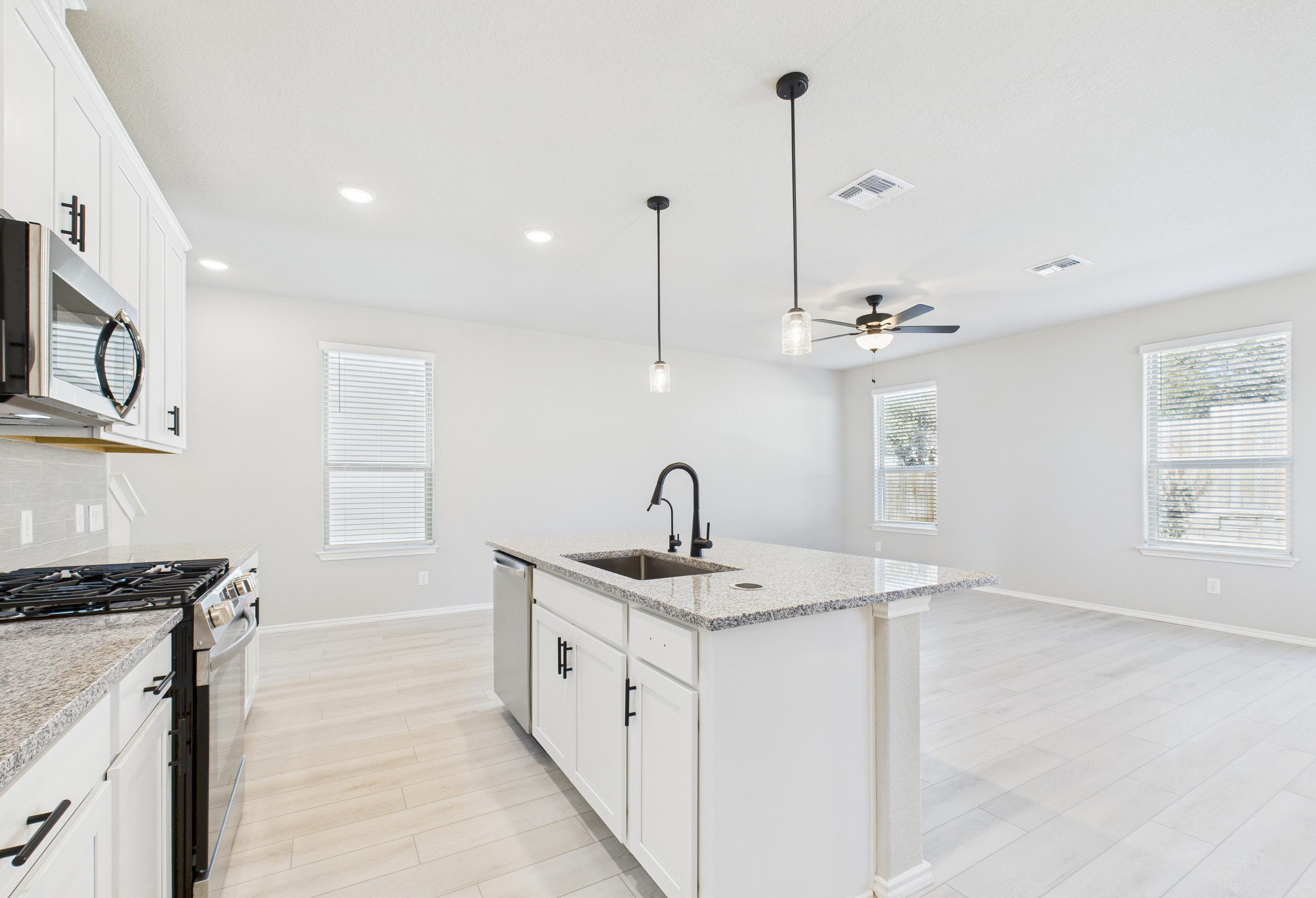 Modern kitchen in The Charlotte A home featuring white cabinets, granite island, and open-concept living in San Antonio.
