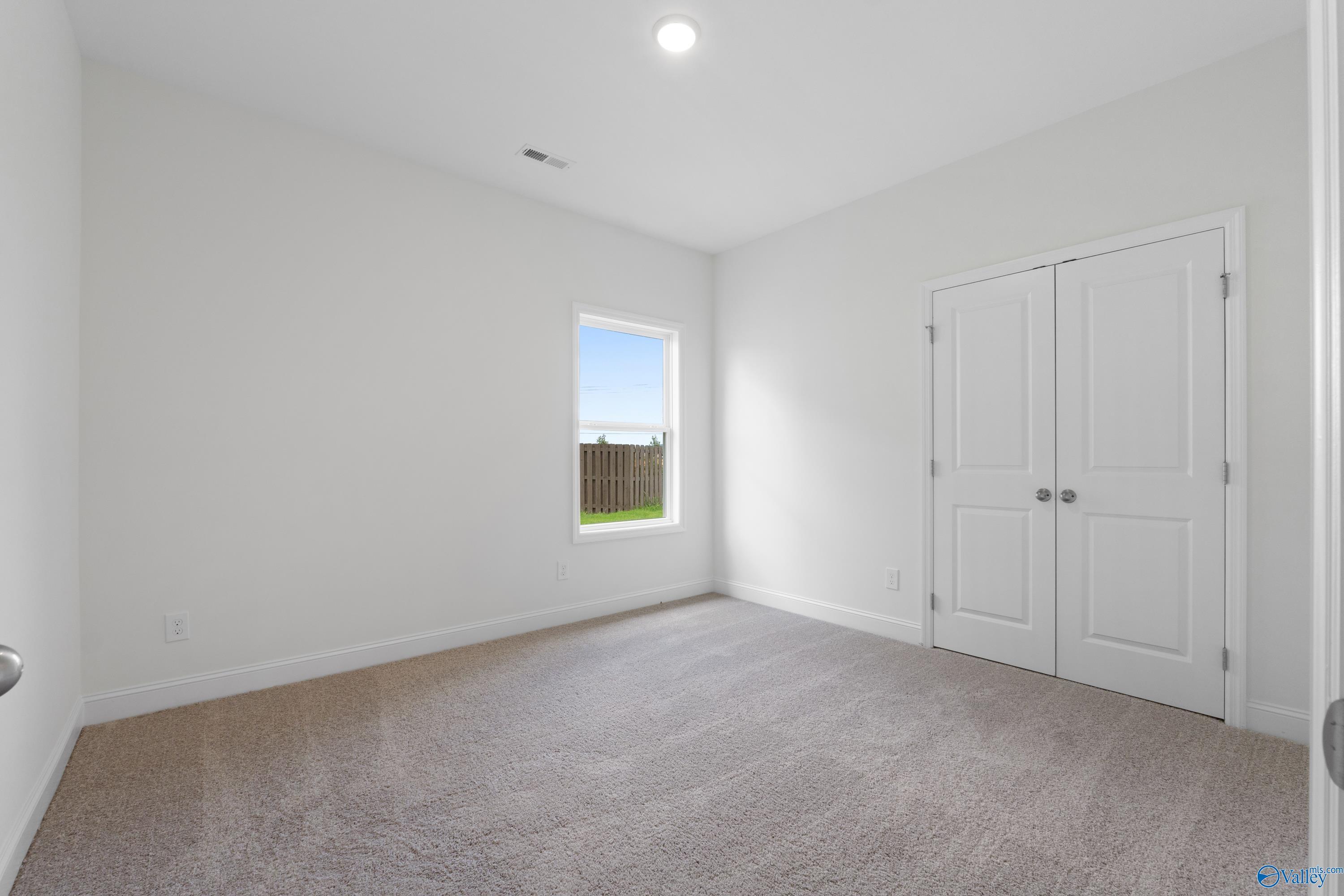 Bright secondary bedroom with neutral carpet and closet in The Everett B floor plan at The Meadows, Athens, Alabama.