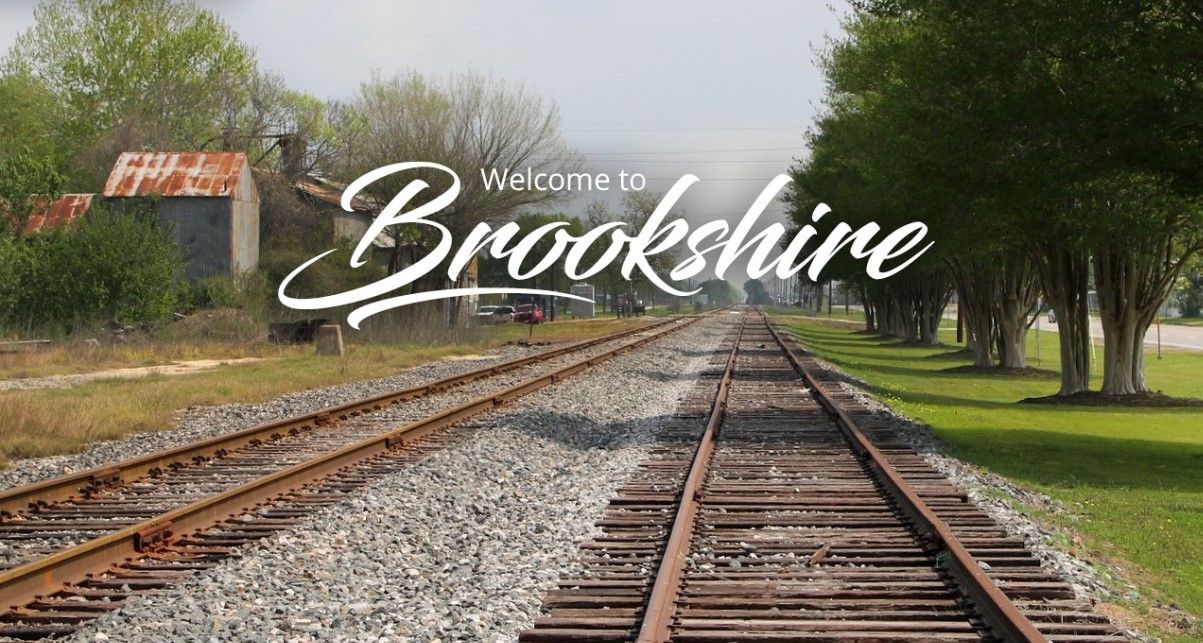 Welcome to Brookshire: Scenic railroad tracks lined with trees and rustic red-roof barn