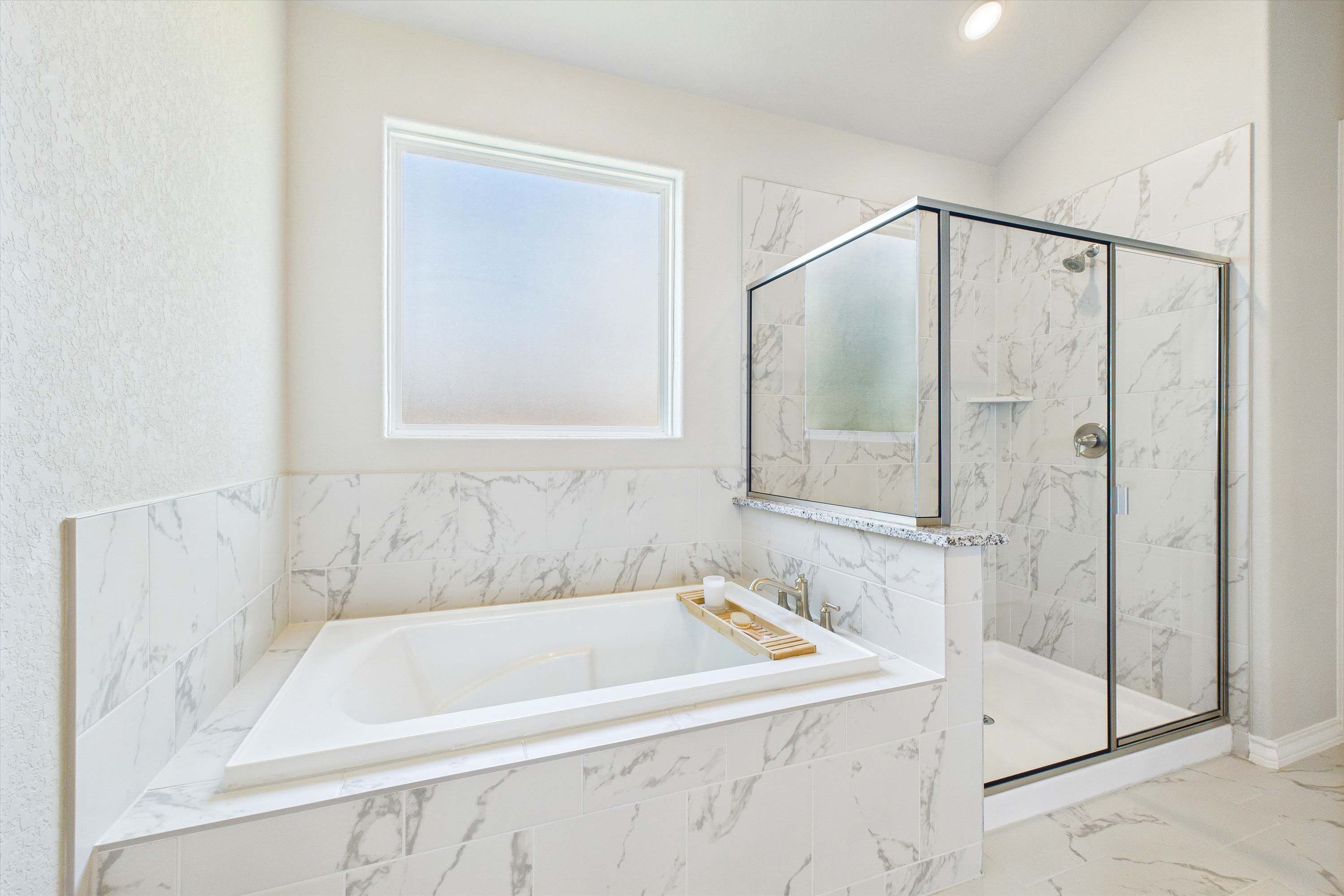 Master suite bathroom in The Foster featuring a soaking tub and walk-in glass shower with marble-look tile surround.