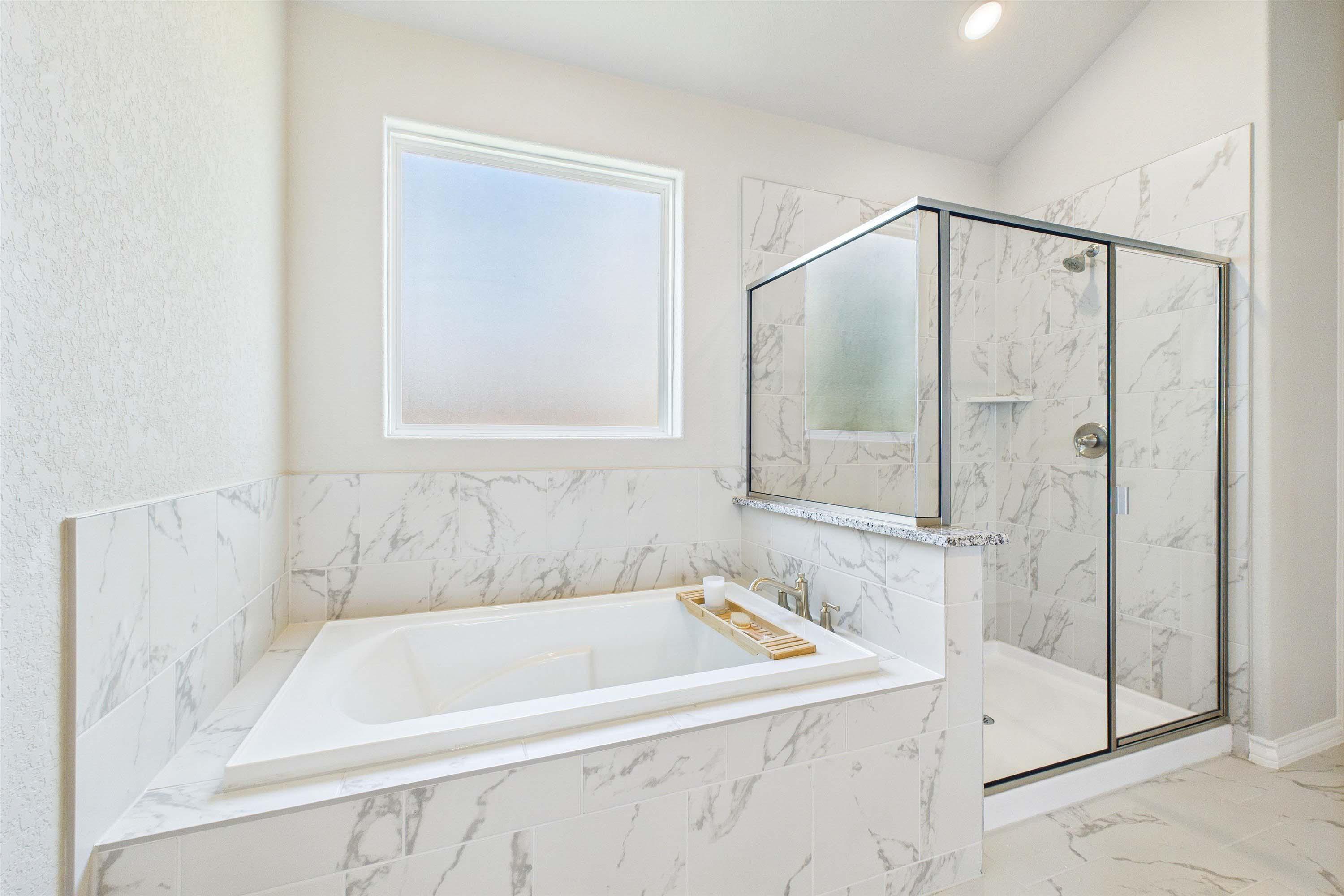 Master suite bathroom in The Foster featuring a soaking tub and walk-in glass shower with marble-look tile surround.