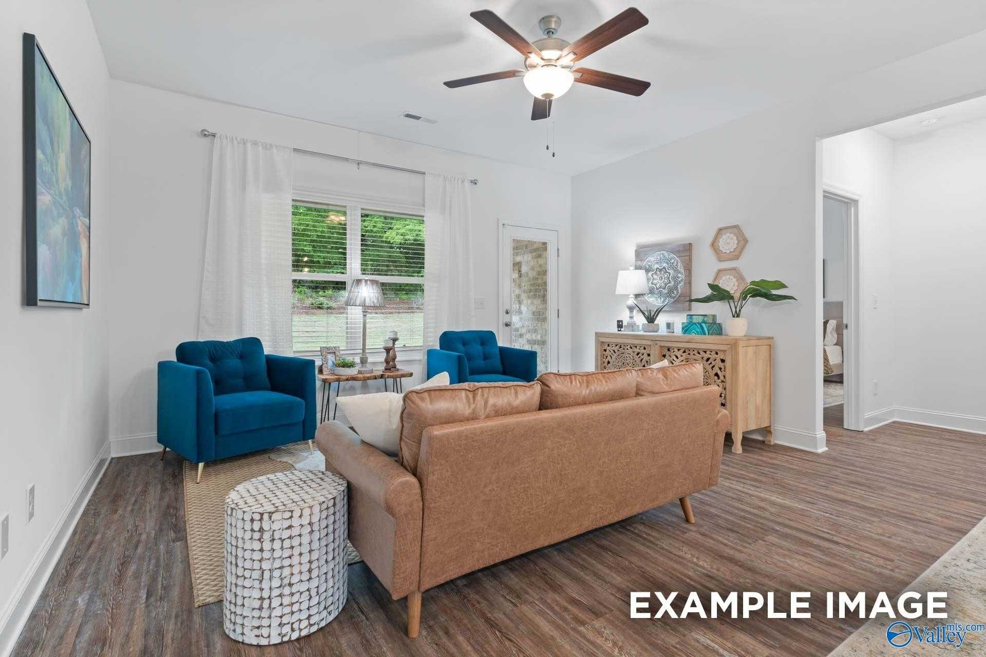 Cozy living room with blue velvet armchairs, tan leather sofa, hardwood floors, and natural light in Davidson Homes The Cumberland, Decatur, Alabama