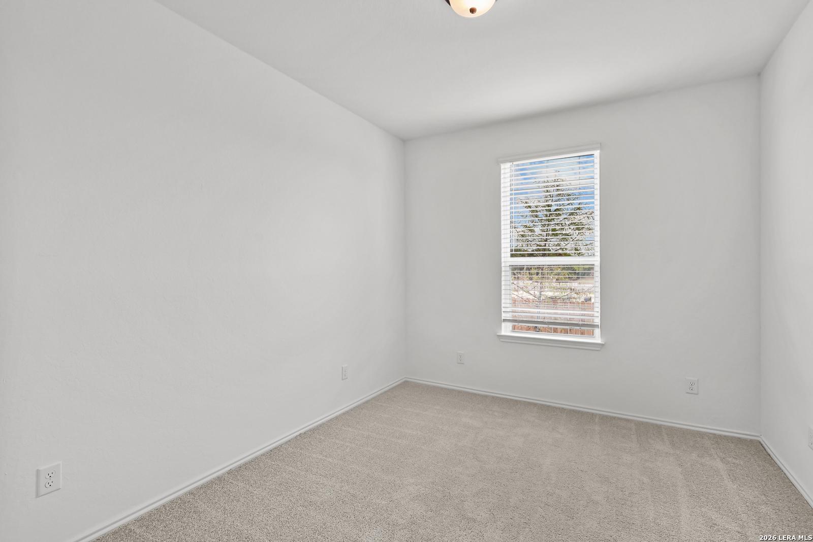 Bright, carpeted bedroom with white walls and a large window in The Gillian C floor plan at Meadows at Oak Creek, TX.