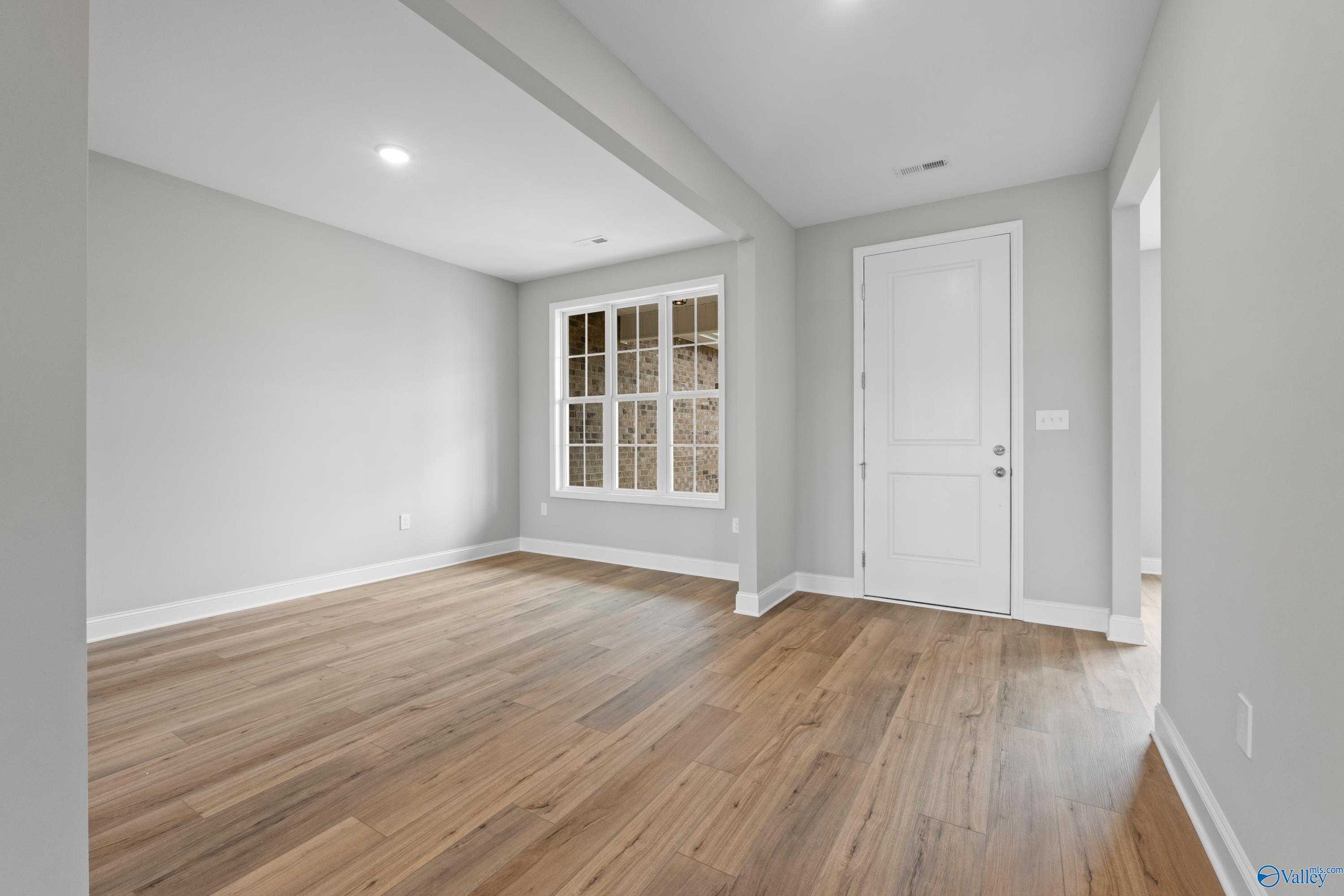 Spacious empty interior room with light hardwood floors, large window, gray walls in Davidson Homes The Finleigh, Meridianville, Alabama
