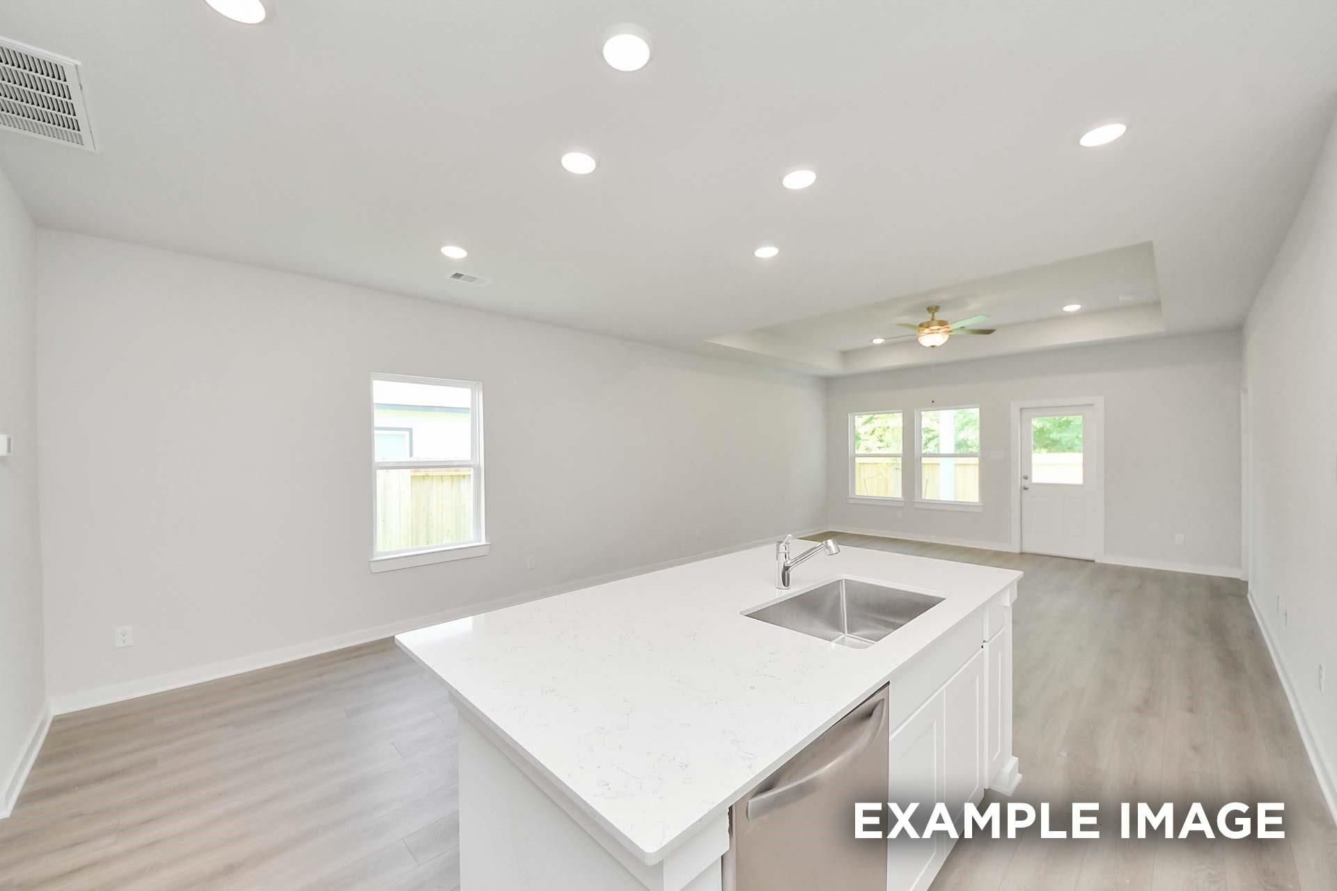 Bright open-concept kitchen with white island, quartz countertops, and luxury vinyl plank flooring in Davidson Homes The Blanco E, Magnolia, TX
