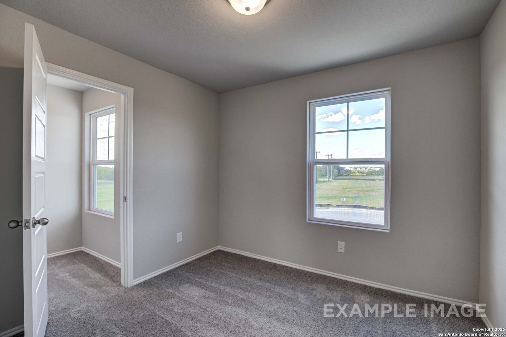 Bright secondary bedroom with gray walls, plush carpet, open door, and window overlooking green fields in Davidson Homes The Blanco C, San Antonio