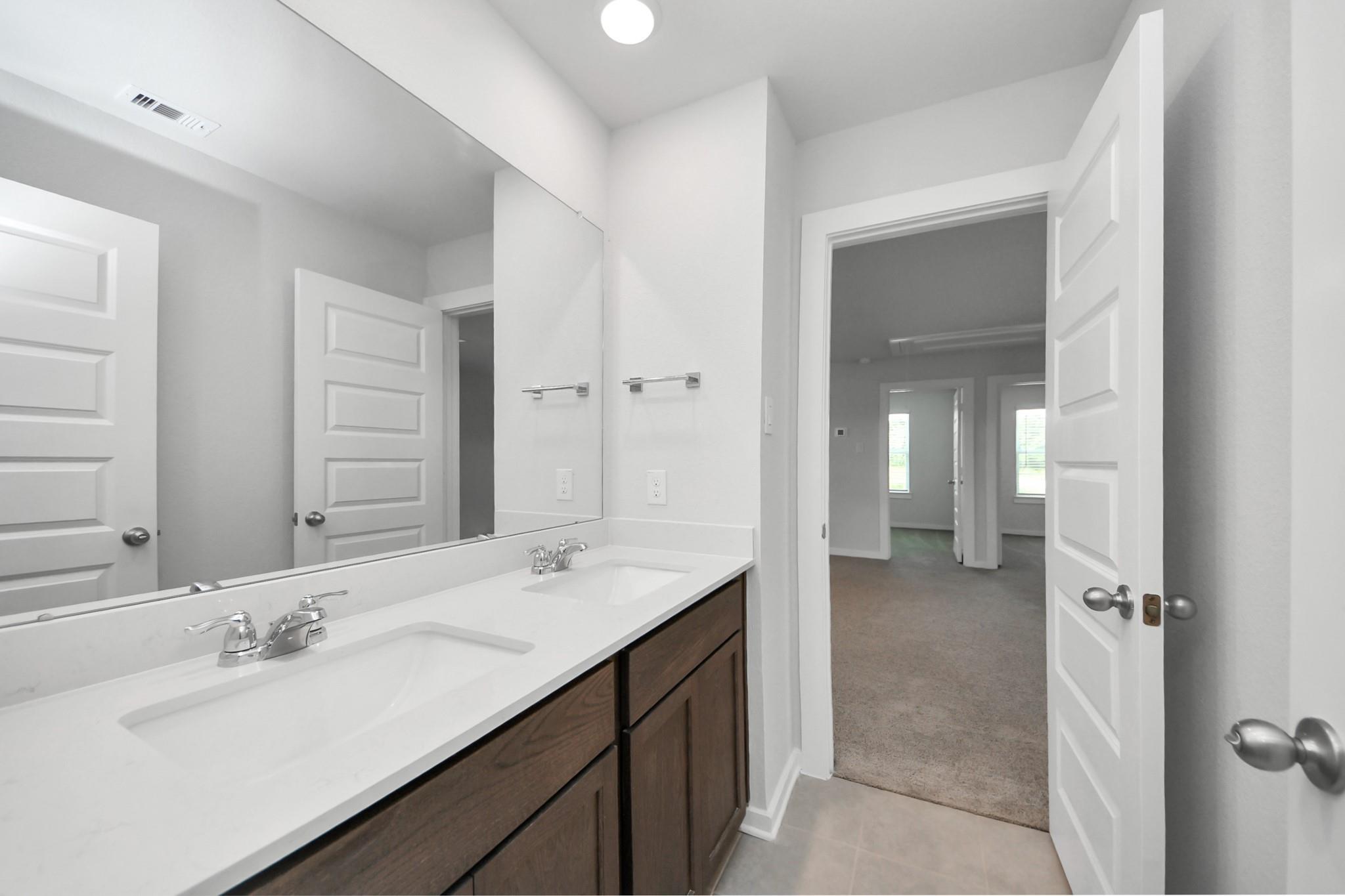 Modern bathroom with dual vanity and dark wood cabinets in The Brazos F floor plan at Liberty Estates, Cleveland, Texas.