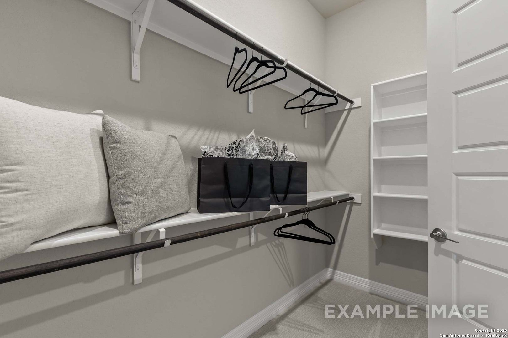 Spacious walk-in closet with white shelves, hanging rods, stacked pillows, and handbag in Davidson Homes The Summerlin B, Castroville, Texas
