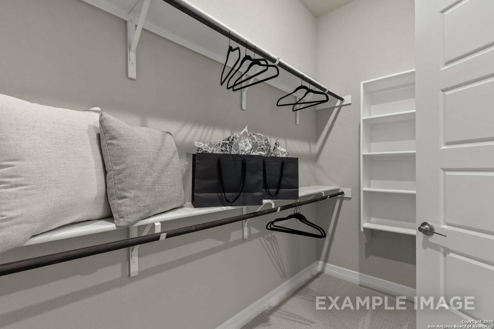 Spacious walk-in closet with white shelves, hanging rods, stacked pillows, and handbag in Davidson Homes The Summerlin B, Castroville, Texas