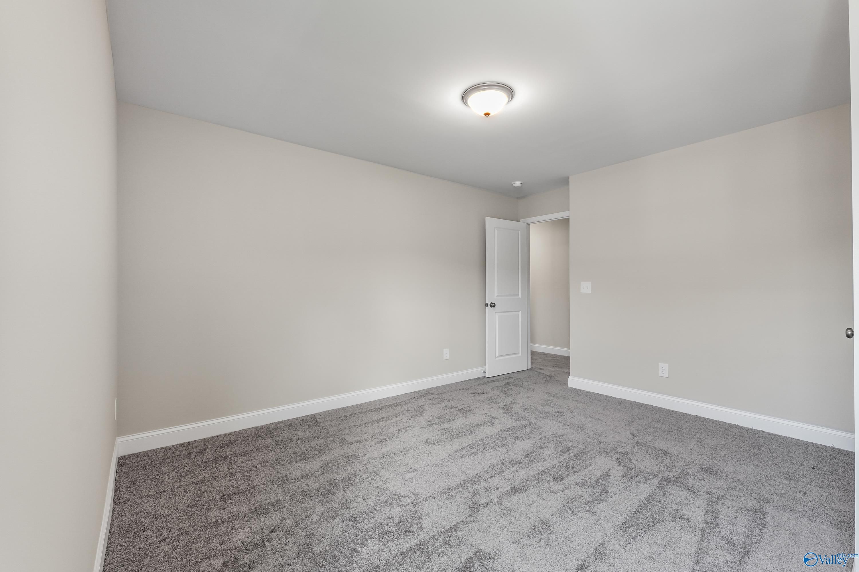 Spacious secondary bedroom with beige walls, gray carpet, and double doors in Evermore Homes The Haven, Owens Cross Roads, Alabama