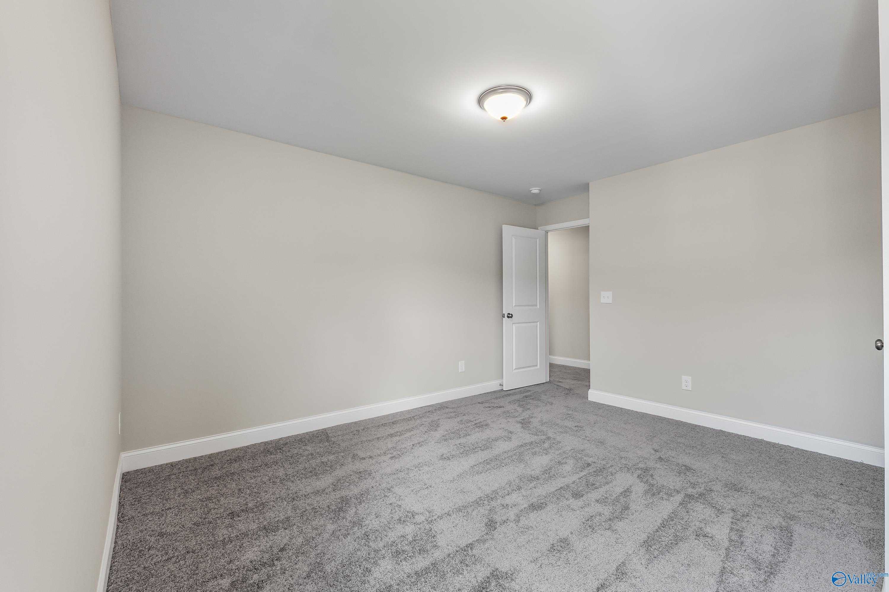Spacious secondary bedroom with beige walls, gray carpet, and double doors in Evermore Homes The Haven, Owens Cross Roads, Alabama
