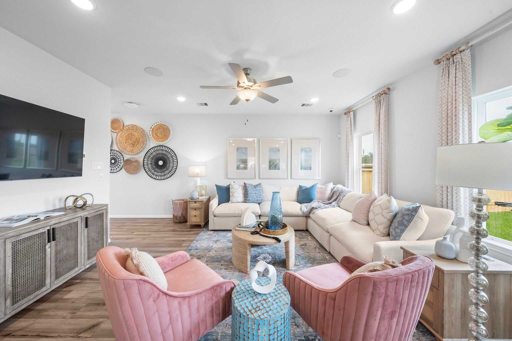 Spacious living room at Spring Branch Crossing in Conroe TX with beige sectional sofa pink velvet chairs woven wall art and hardwood floors