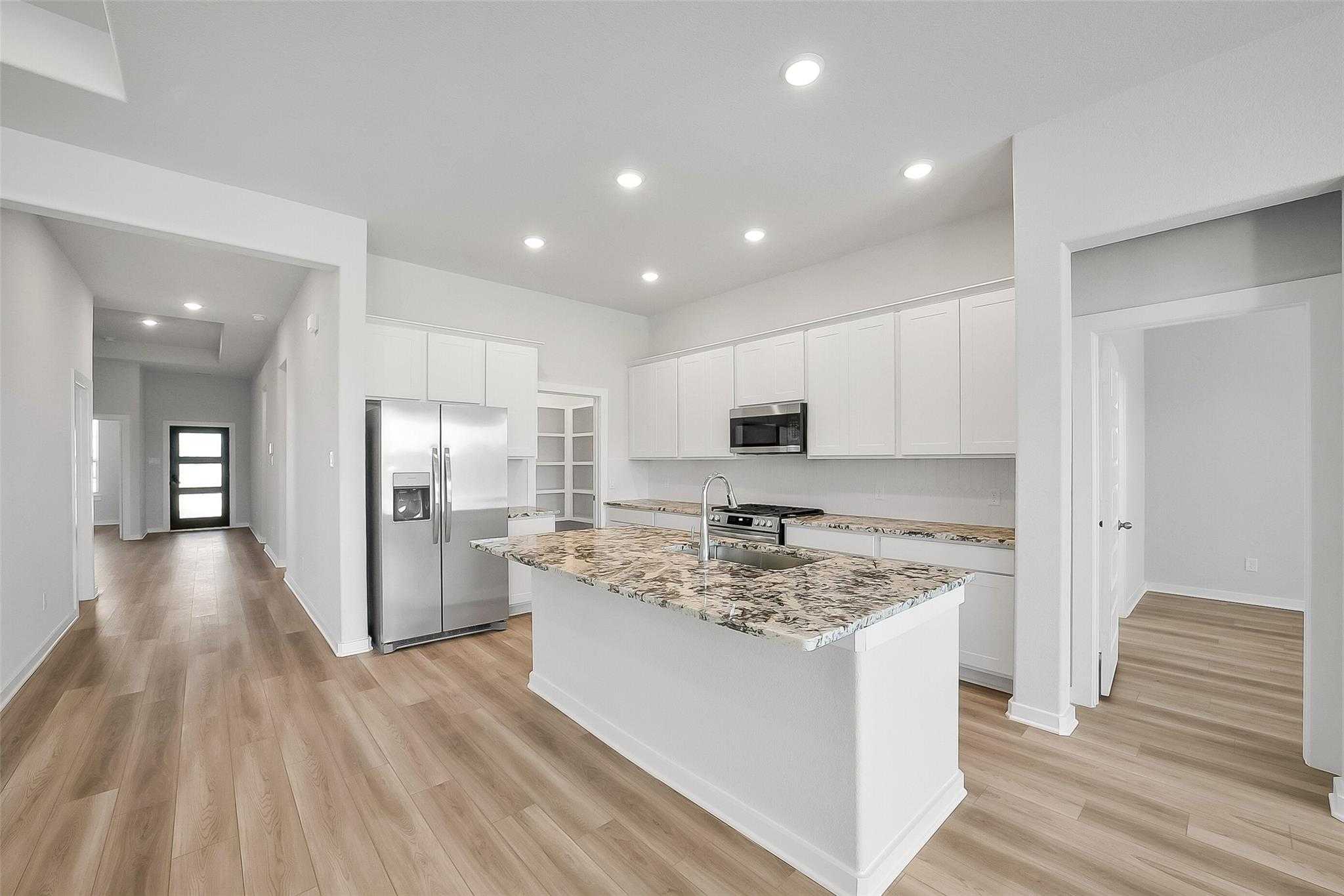 Modern open kitchen with white cabinets, swirled granite island, stainless fridge in Davidson Homes Acadia A, Katy TX