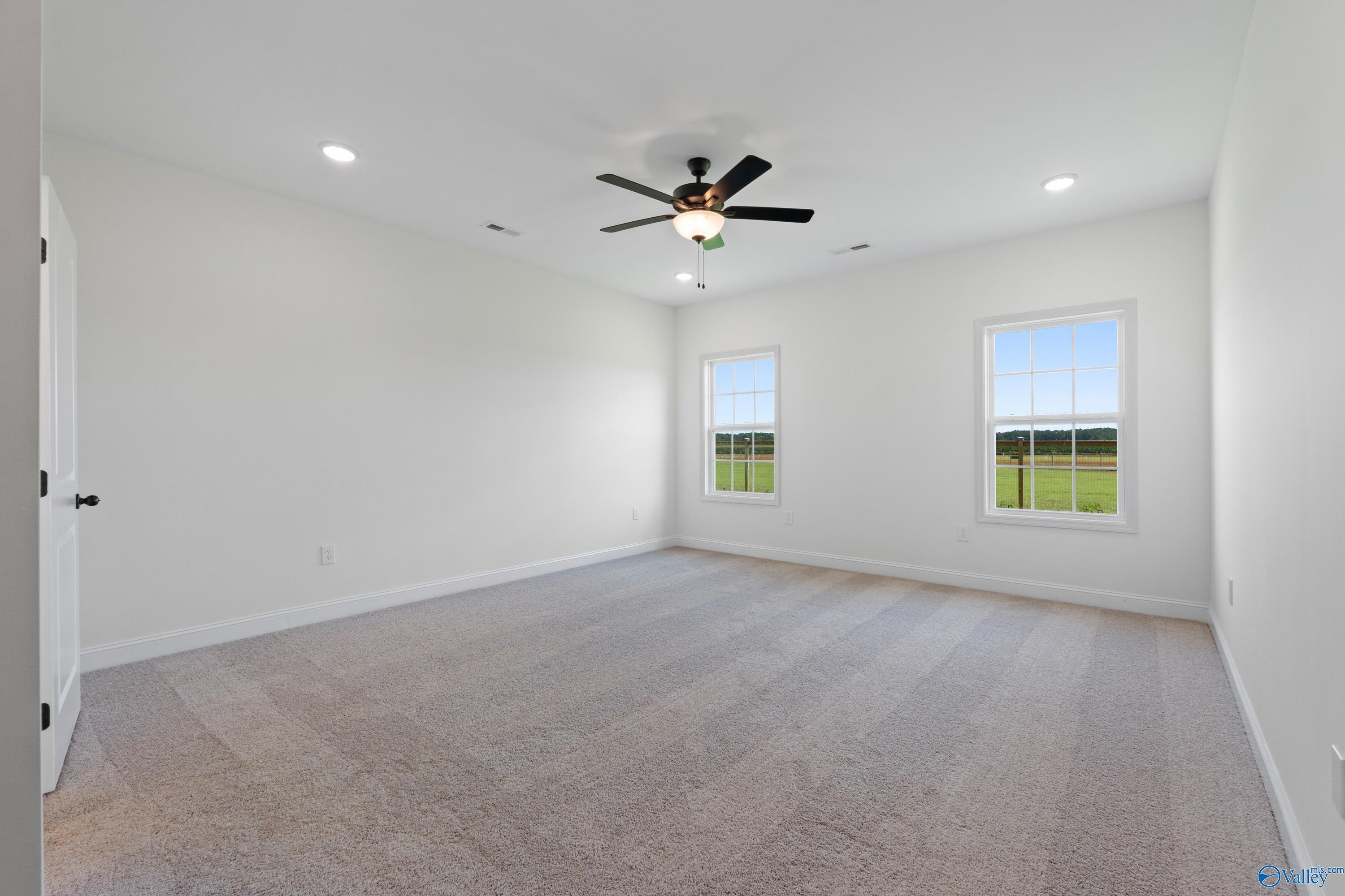 Spacious empty bedroom with ceiling fan, carpet flooring, and windows overlooking green pasture in The Rockford B, Toney, Alabama