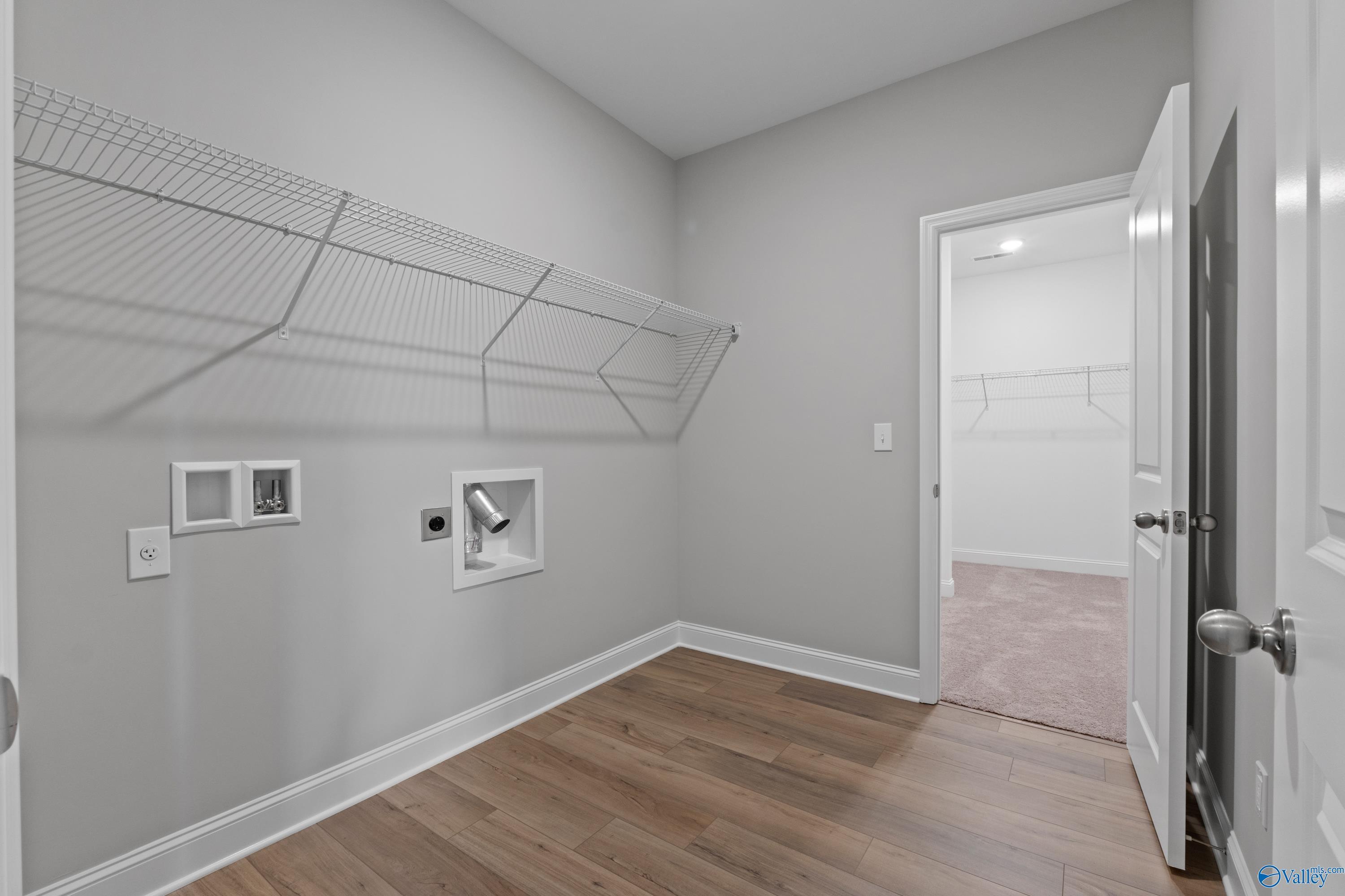 Modern laundry room with wire shelving, washer/dryer hookups, and adjacent bedroom access in Davidson Homes The Everett B, Ivy Hills, Toney, Alabama