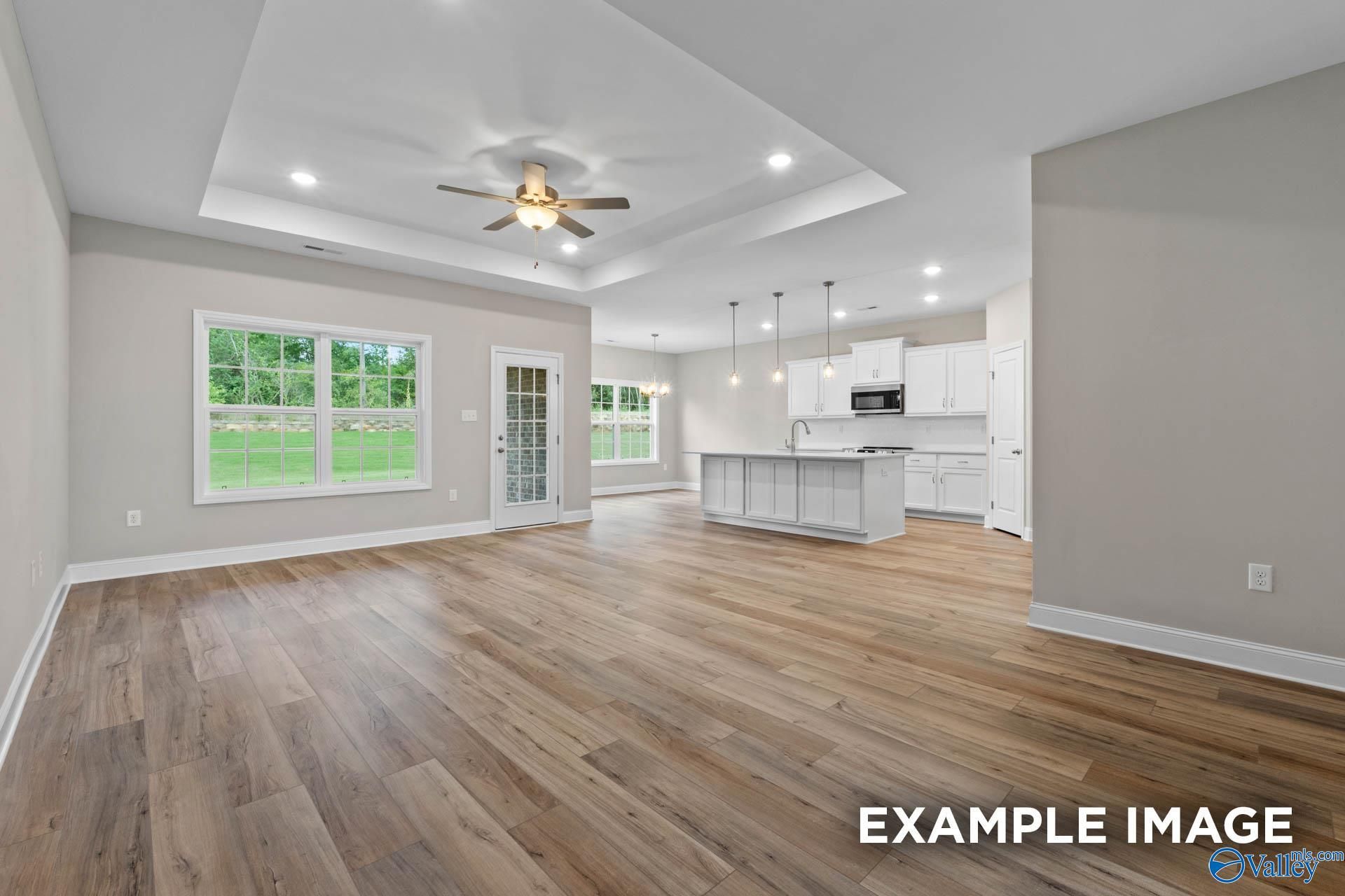 Open-concept kitchen and living area with white island, hardwood floors, French doors, and large windows in Davidson Homes The Montgomery, Meridianville, Alabama
