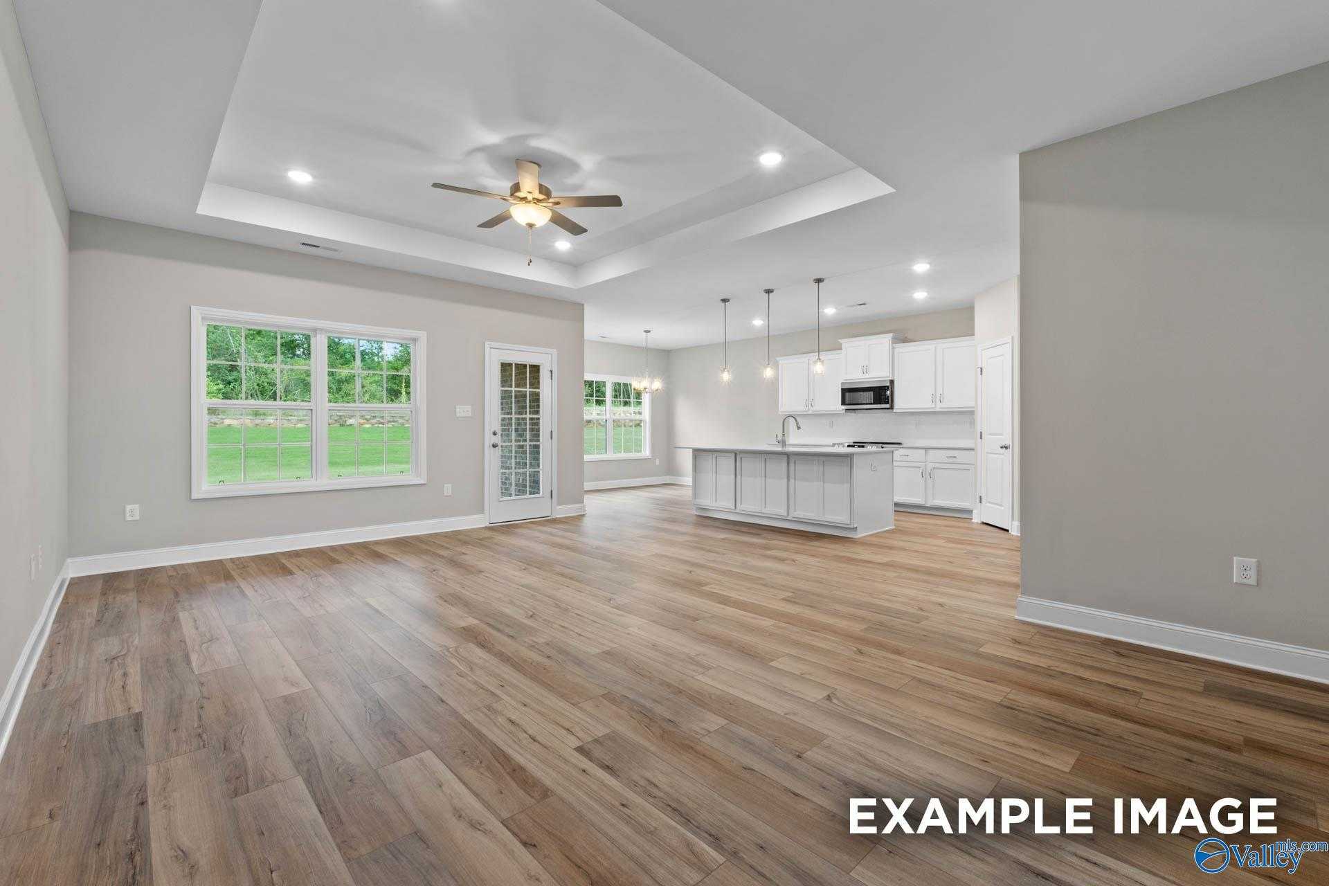Open-concept kitchen and living area with white island, hardwood floors, French doors, and large windows in Davidson Homes The Montgomery, Meridianville, Alabama