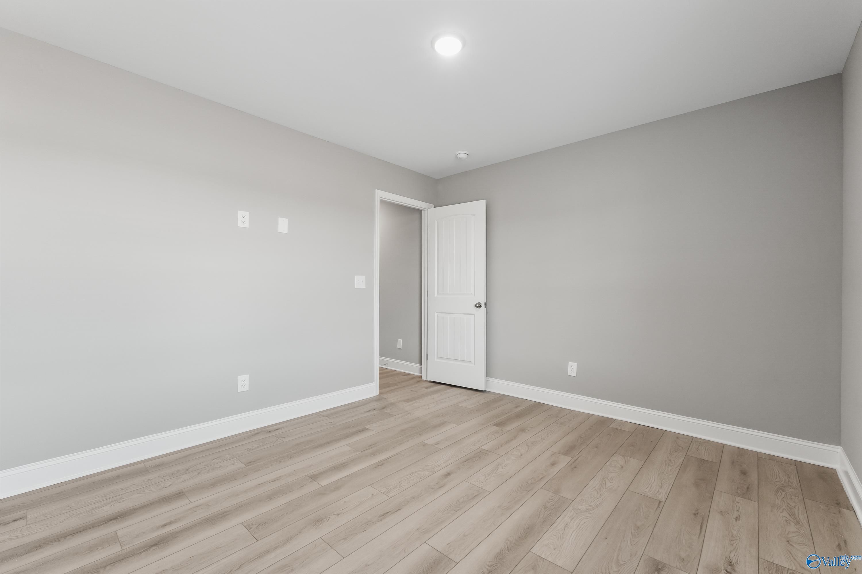 Spacious bedroom with light gray walls, white door, outlets, and hardwood floors in Davidson Homes The Everett B, Athens, AL