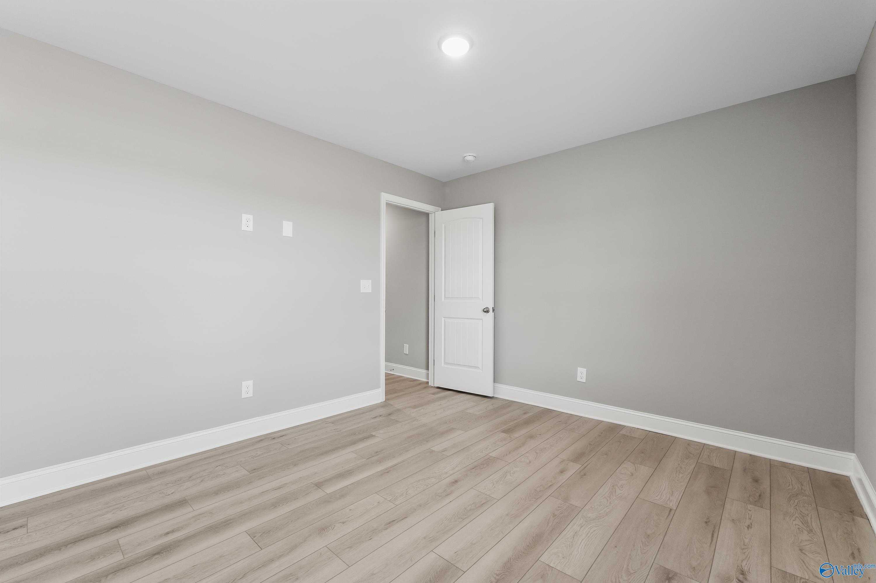 Spacious secondary bedroom with light gray walls, white door, and hardwood floors in Davidson Homes The Everett B, Athens AL