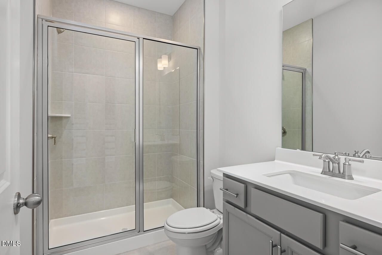 Modern bathroom featuring glass shower enclosure, gray vanity with single sink, and toilet in The Hickory II B by Davidson Homes, Lillington, NC
