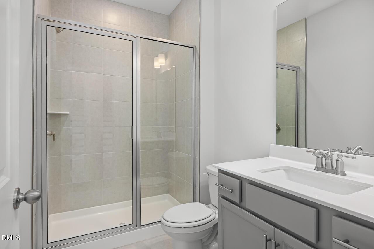 Modern bathroom featuring glass shower enclosure, gray vanity with single sink, and toilet in The Hickory II B by Davidson Homes, Lillington, NC