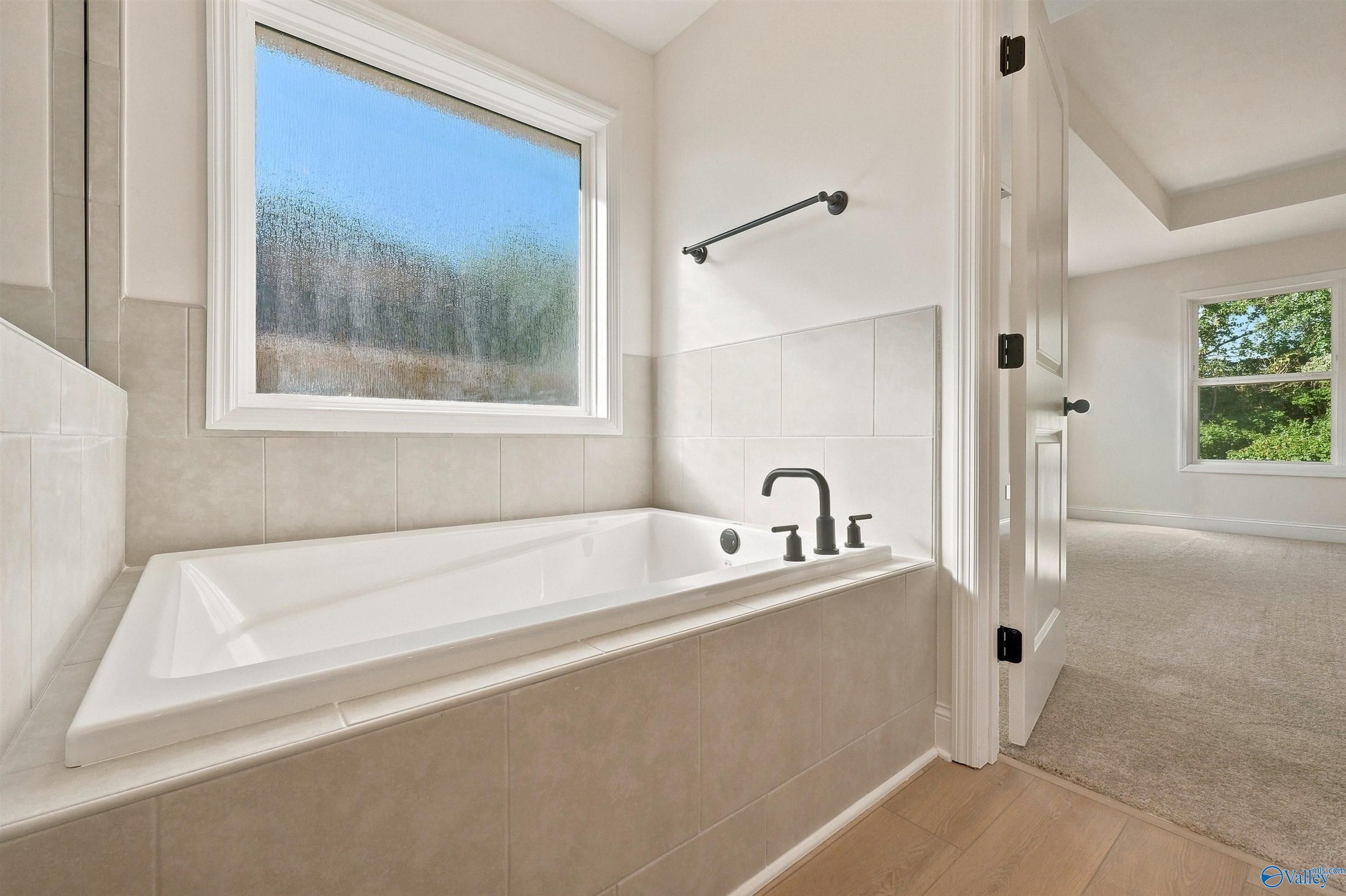 Soaking tub with tile surround and modern matte black fixtures in a Chelsea C floor plan home in Creek Grove, Alabama.