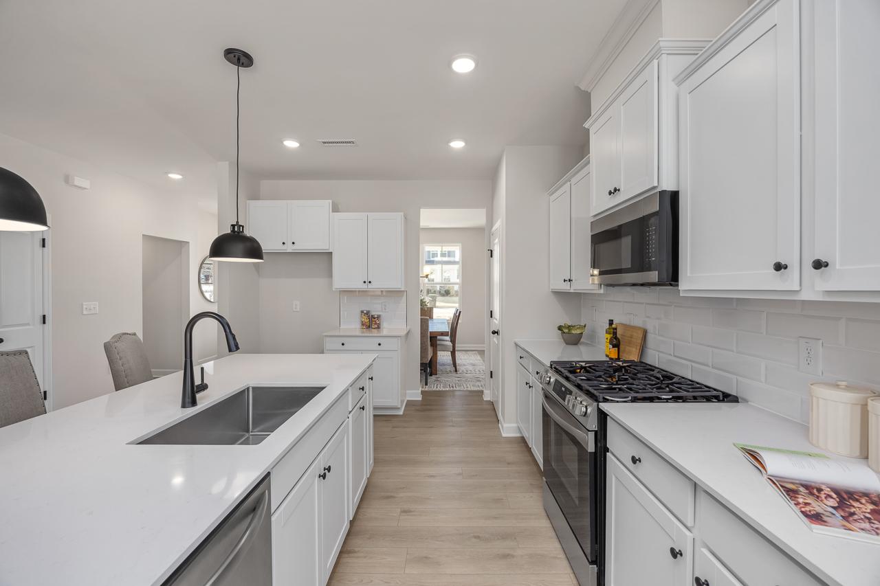 Modern kitchen with white cabinets, quartz countertops, and stainless steel appliances at Retreat at North Main in Lillington.