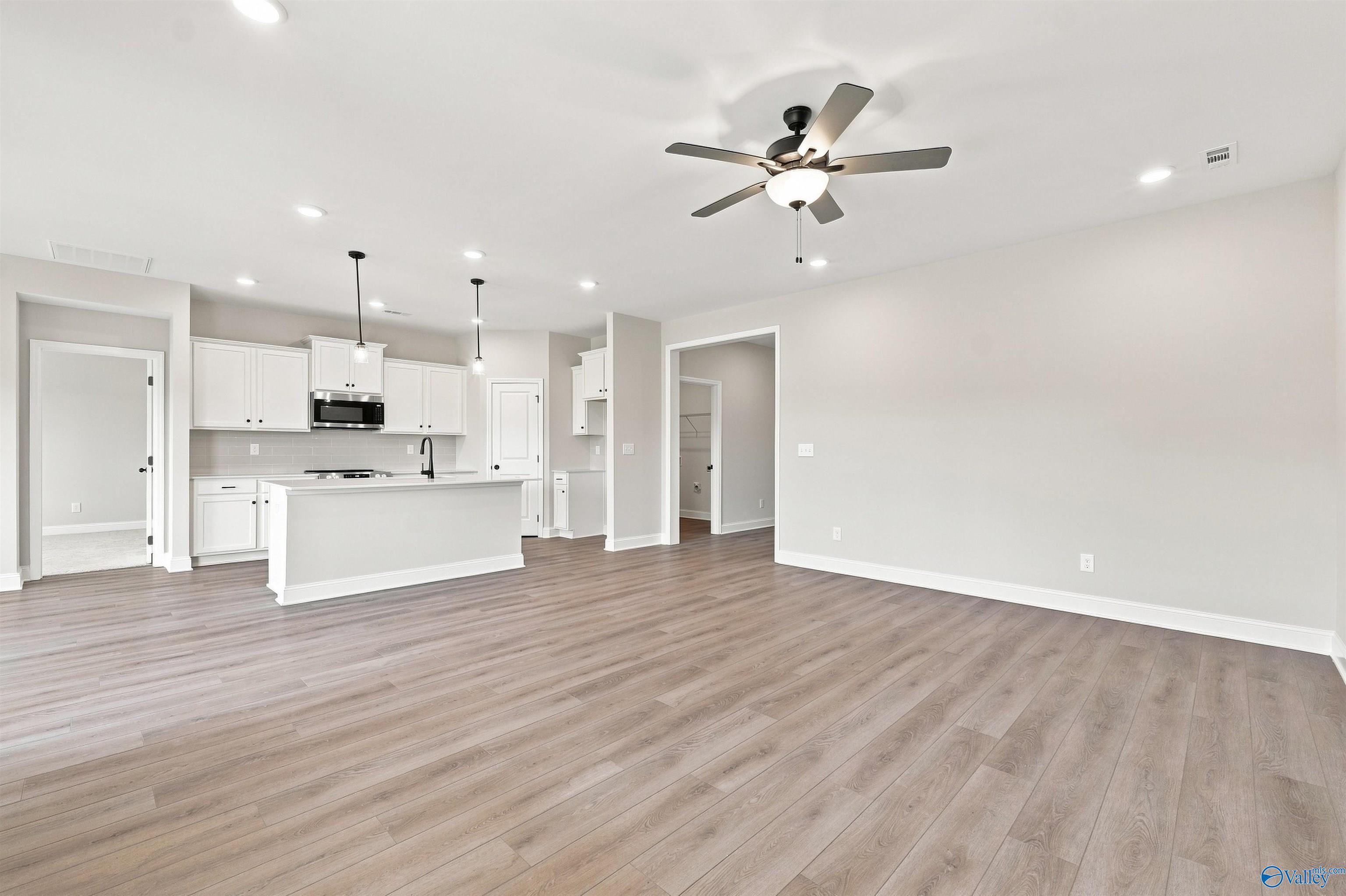 Open-concept living area with luxury vinyl plank flooring, white kitchen island, and ceiling fan in Davidson Homes Everett B plan