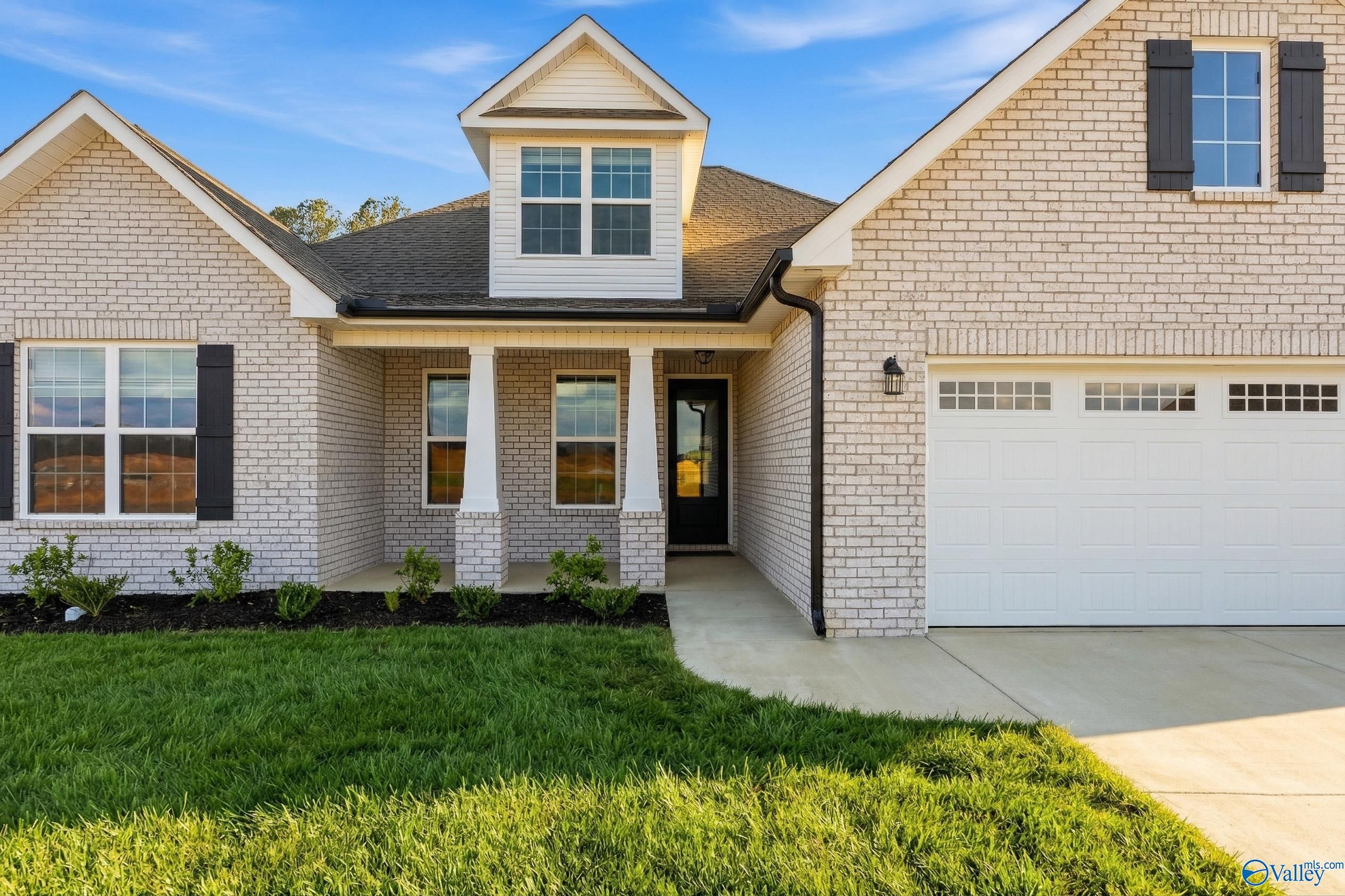 Beige brick 1.5-story Davidson Homes Rockford with covered porch, dormer window, 3-car garage, and landscaped yard in Cain Park, Hartselle, Alabama